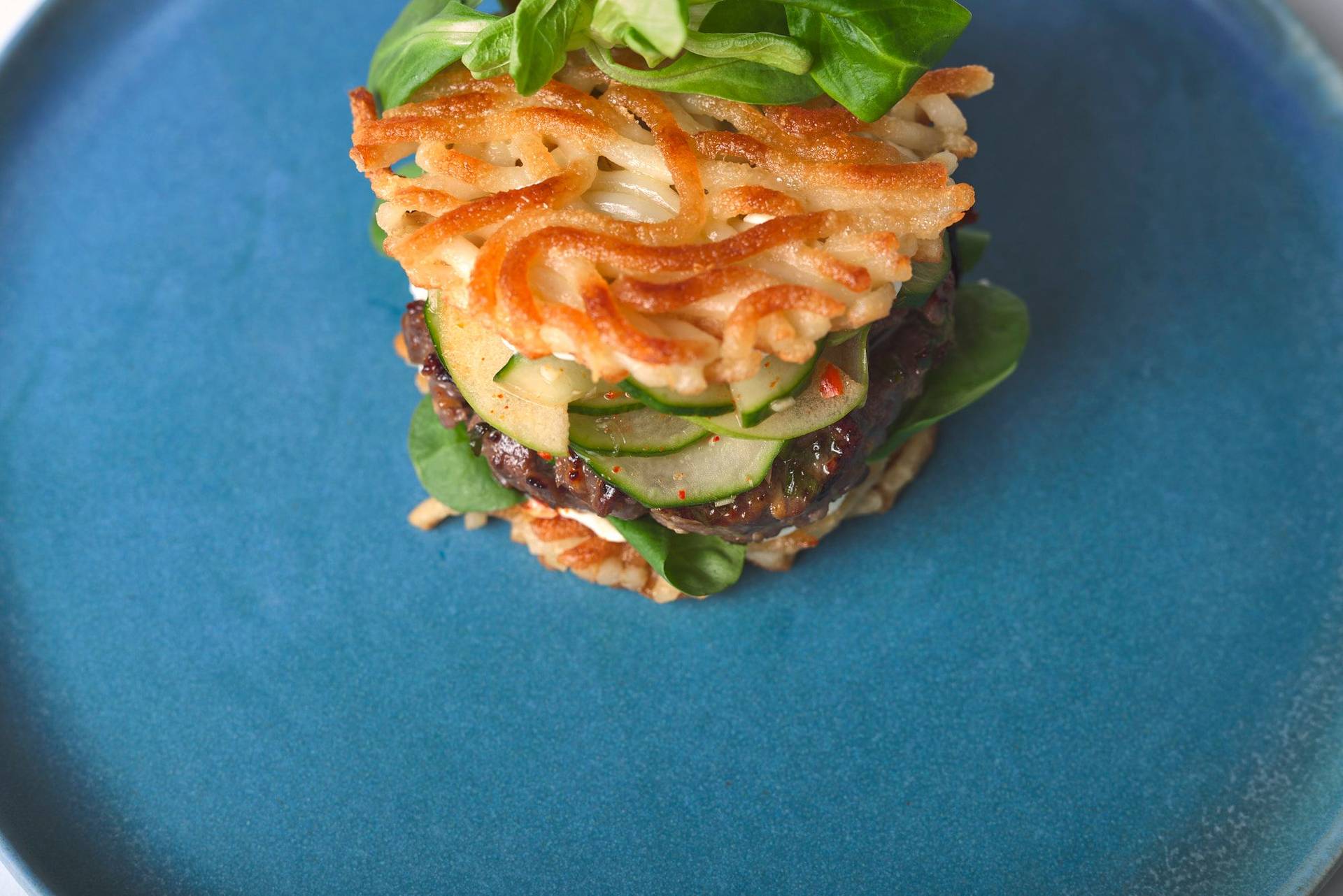 bulgogi beef burger with cucumber kimchi and udon noodle buns on a blue ceramic plate
