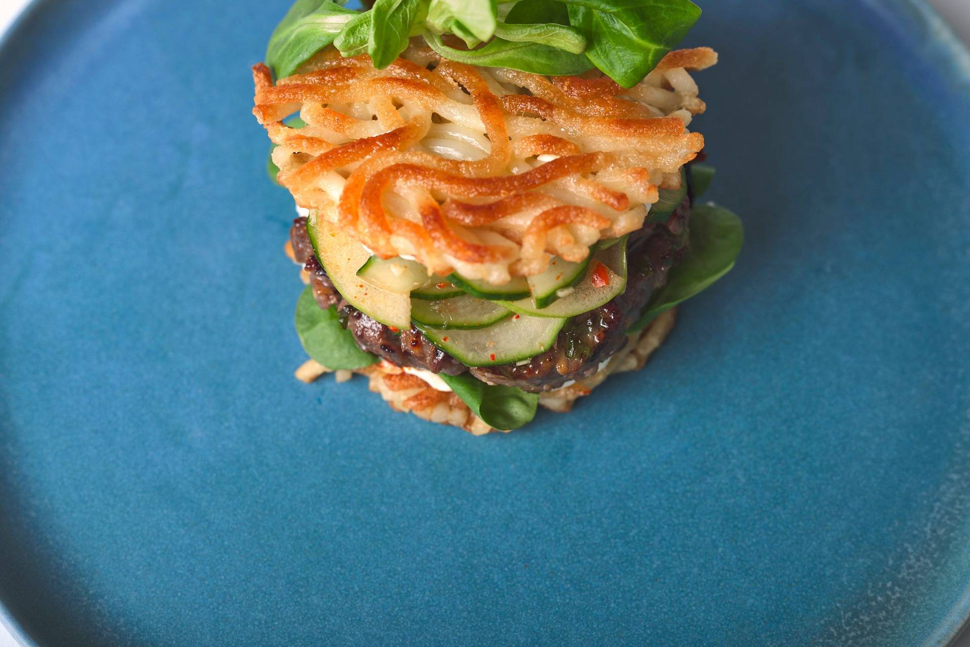 bulgogi beef burger mit gurken kimchi und udon nudel buns auf einem blauen keramik teller