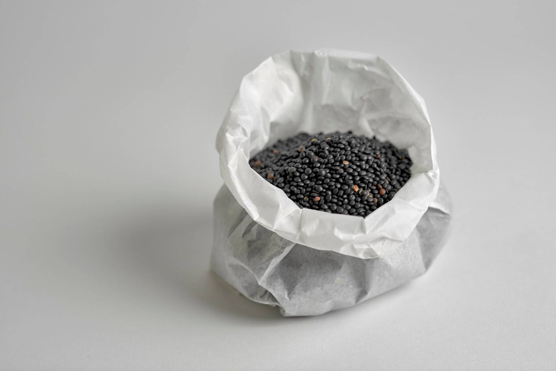 black beluga lentils in a paper bag on white background