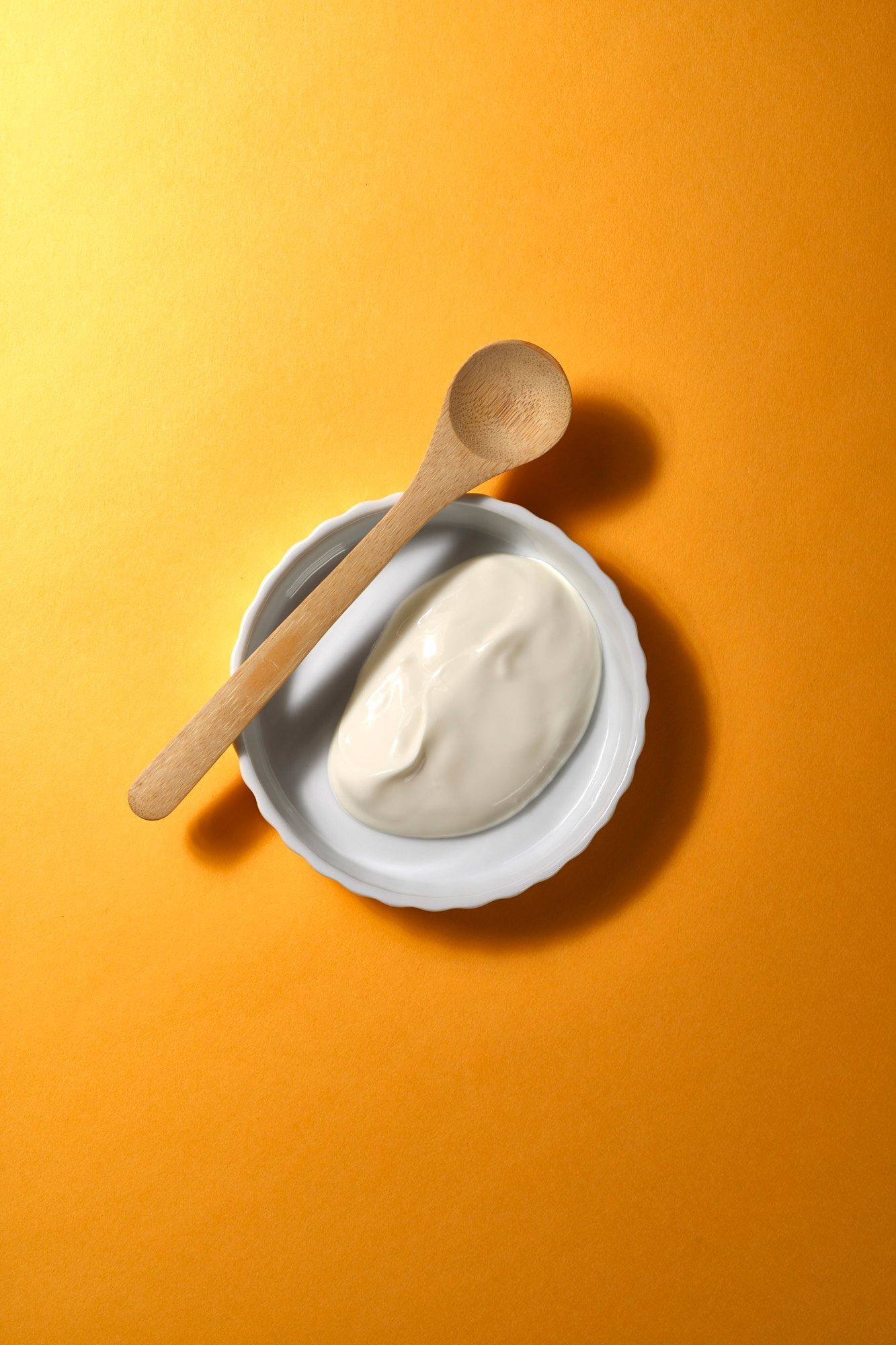creme fraiche in a white bowl with wooden spoon with yellow background