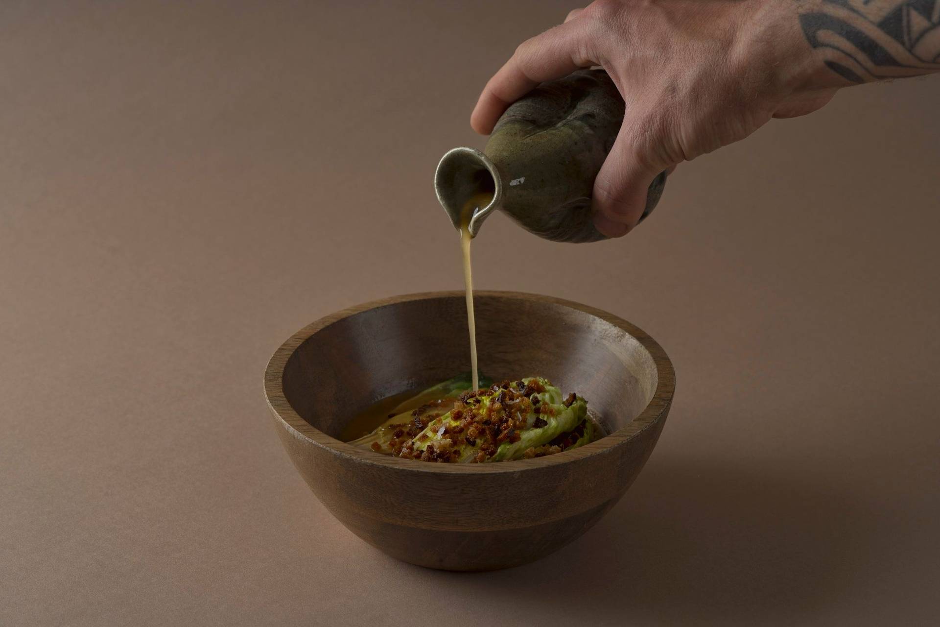 römersalat mit miso sud und sauerteig in einer holzschale mit braunem hintergrund