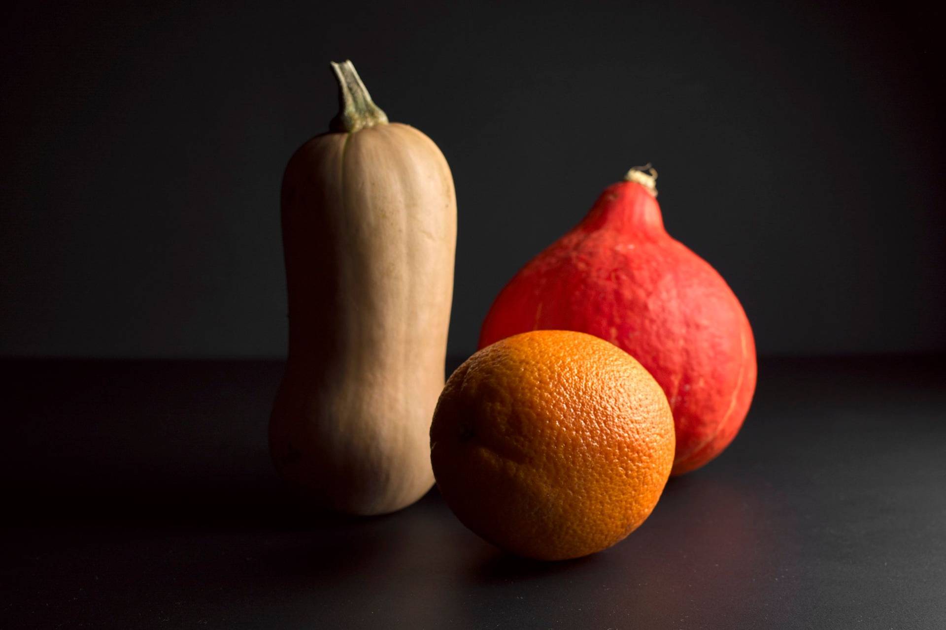 two pumpkins and one orange on black background