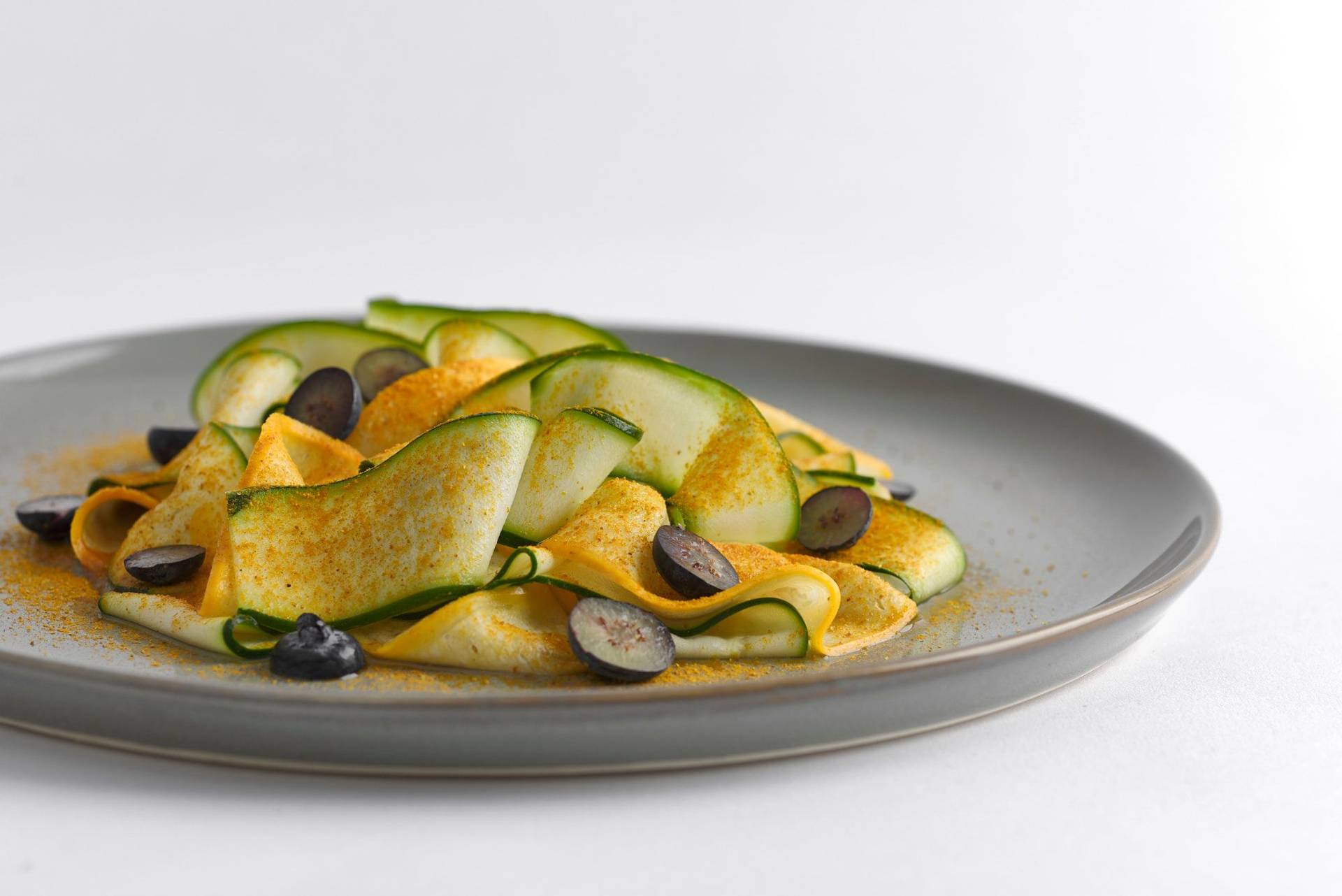 courgette with almond butter madras curry and blueberries on a gray plate with white background