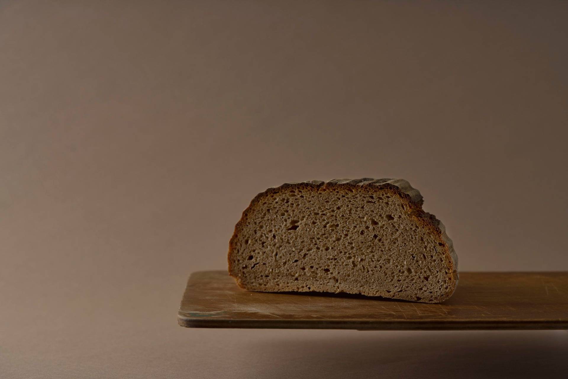 a loaf of rye sourdough bread on a wooden board with brown background