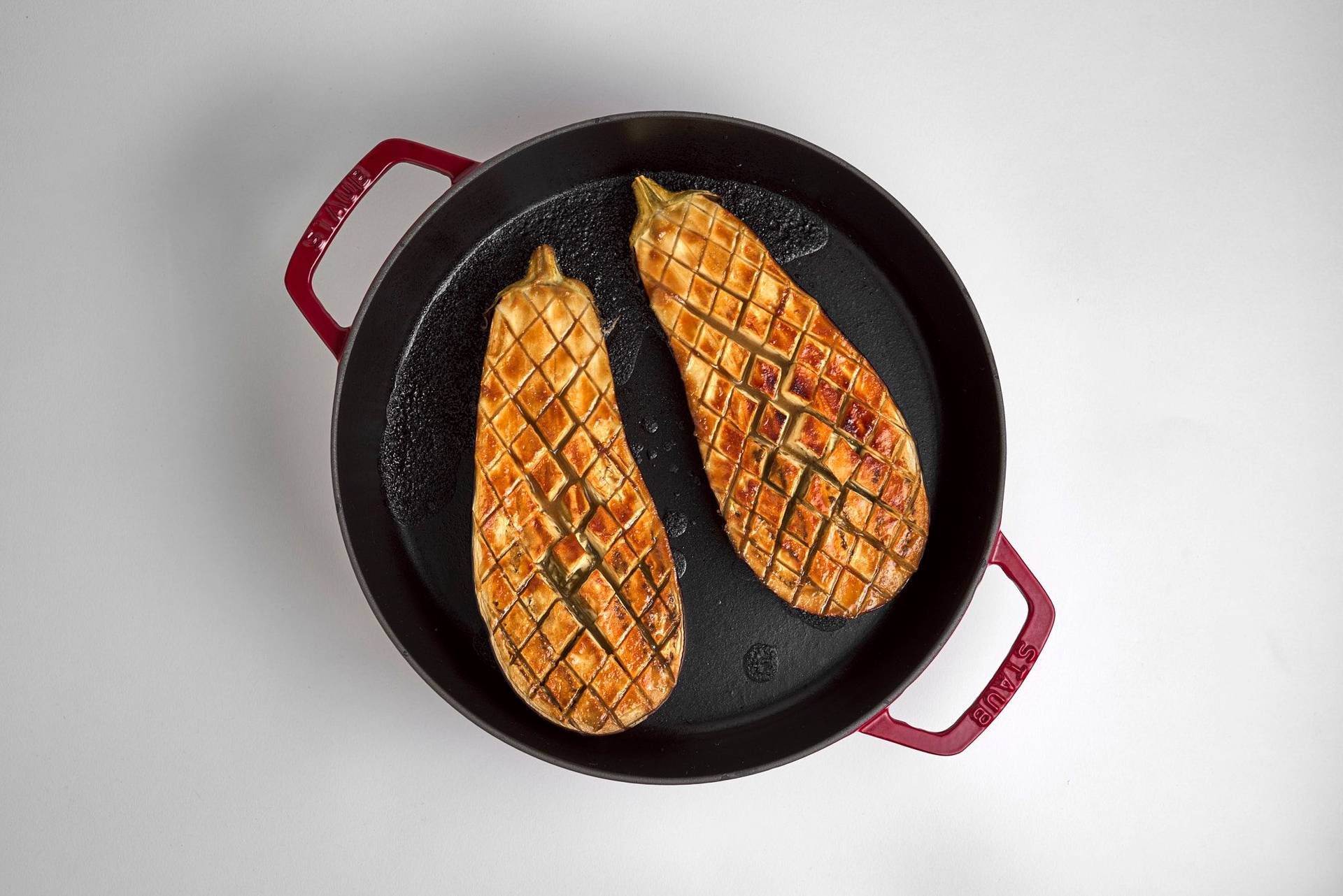 miso roasted eggplantin a red staub cast iron pot on white background