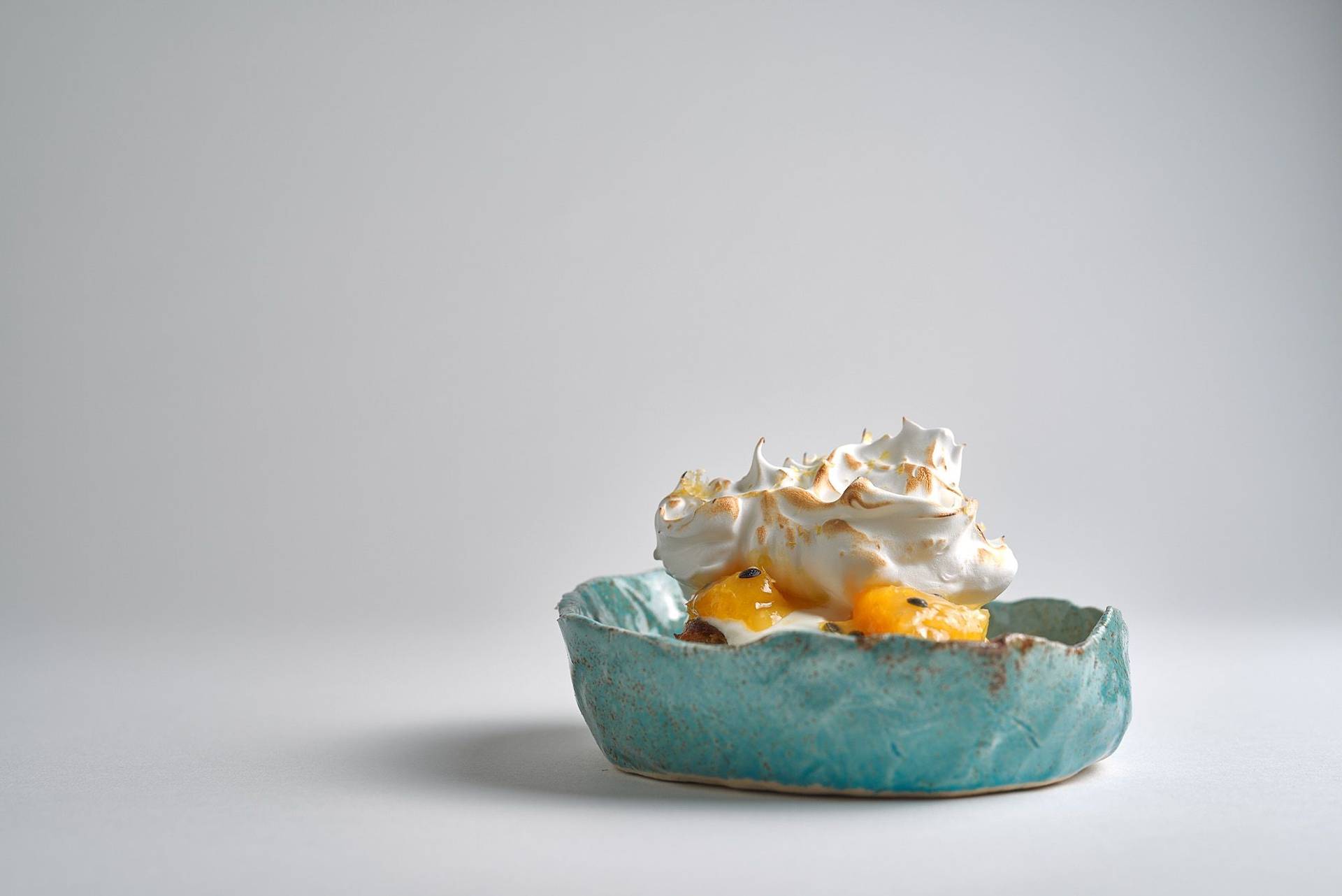 Passionsfrucht Baiser Dessert in blauer Keramikschale vor weißem Hintergrund
