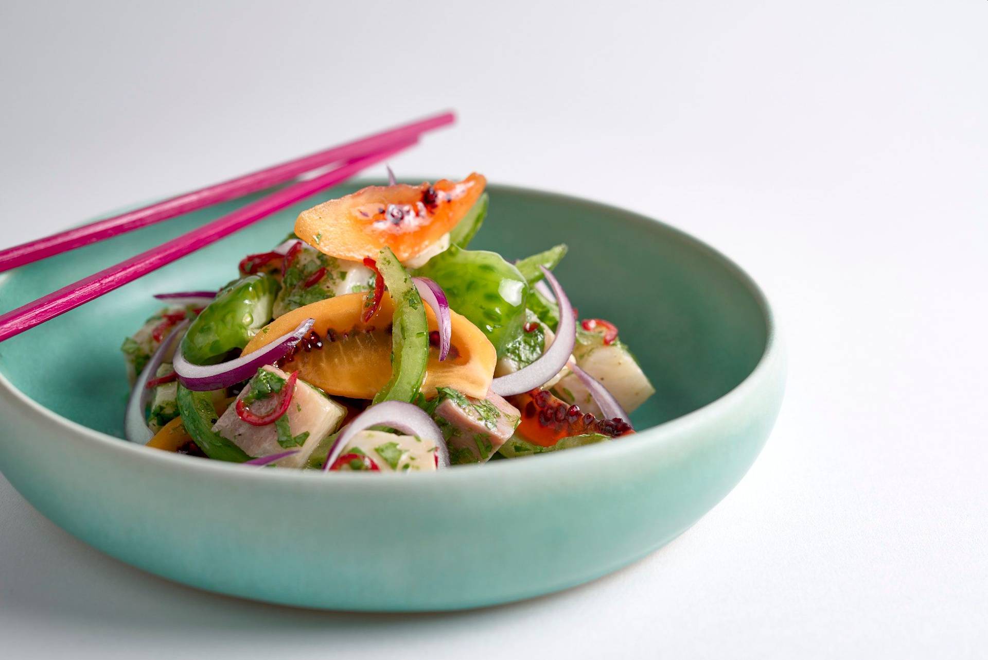 kingfish ceviche with tomatoes in a turquoise ceramic bowl on white background