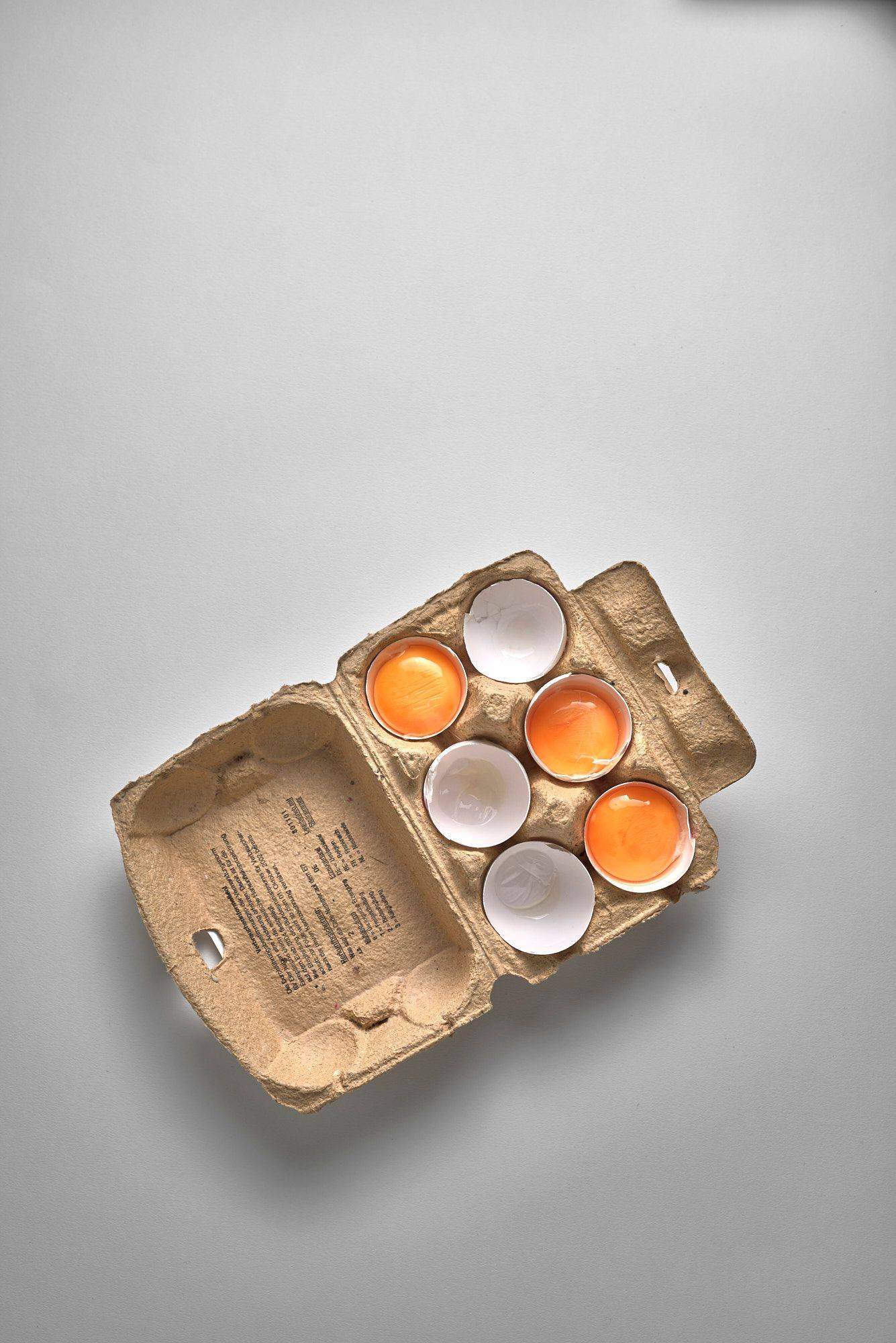 drei aufgeschlagene eier in einem eierkarton auf weißem hintergrund