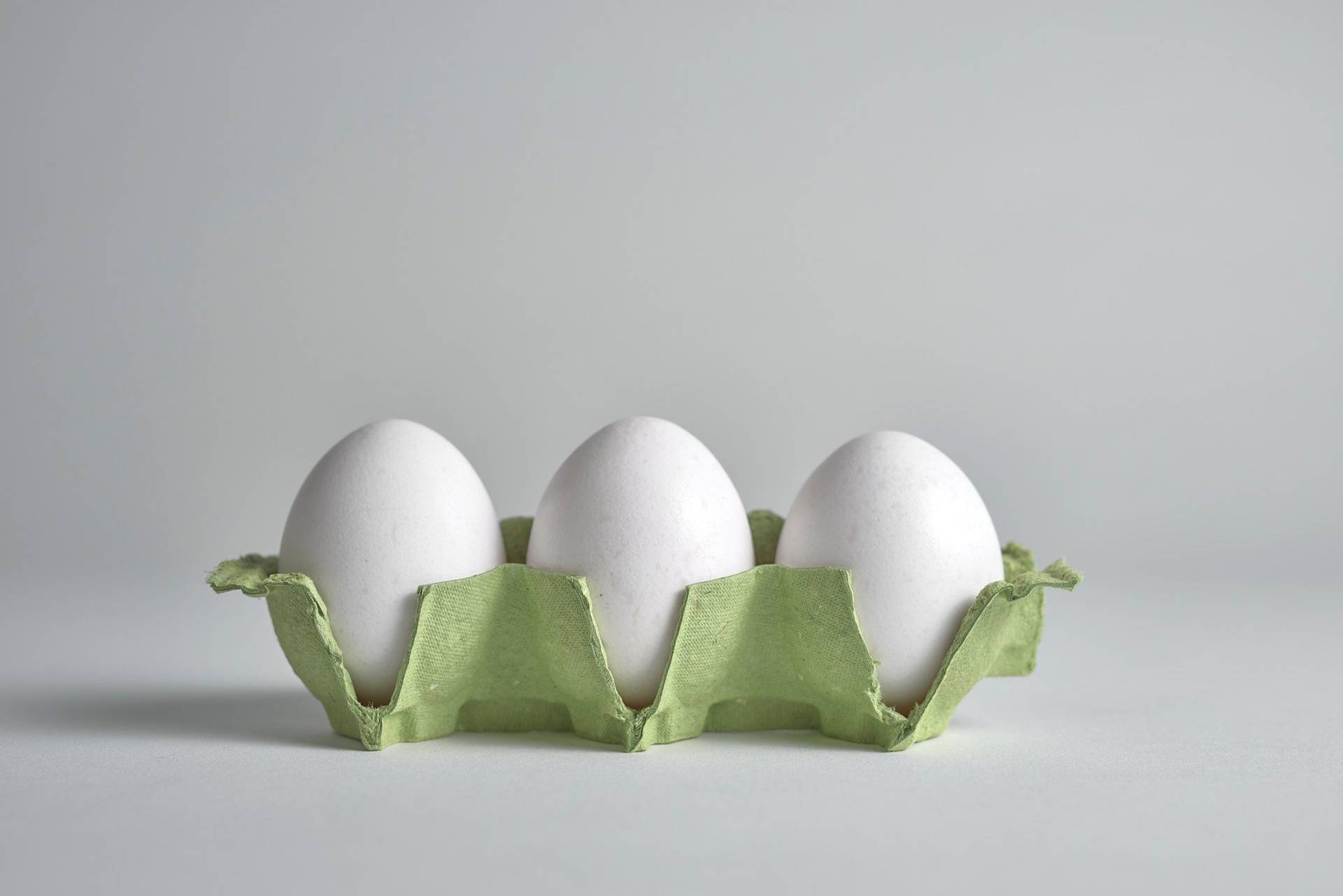 drei weiße eier in einem grünen eierkarton auf weißem hintergrund