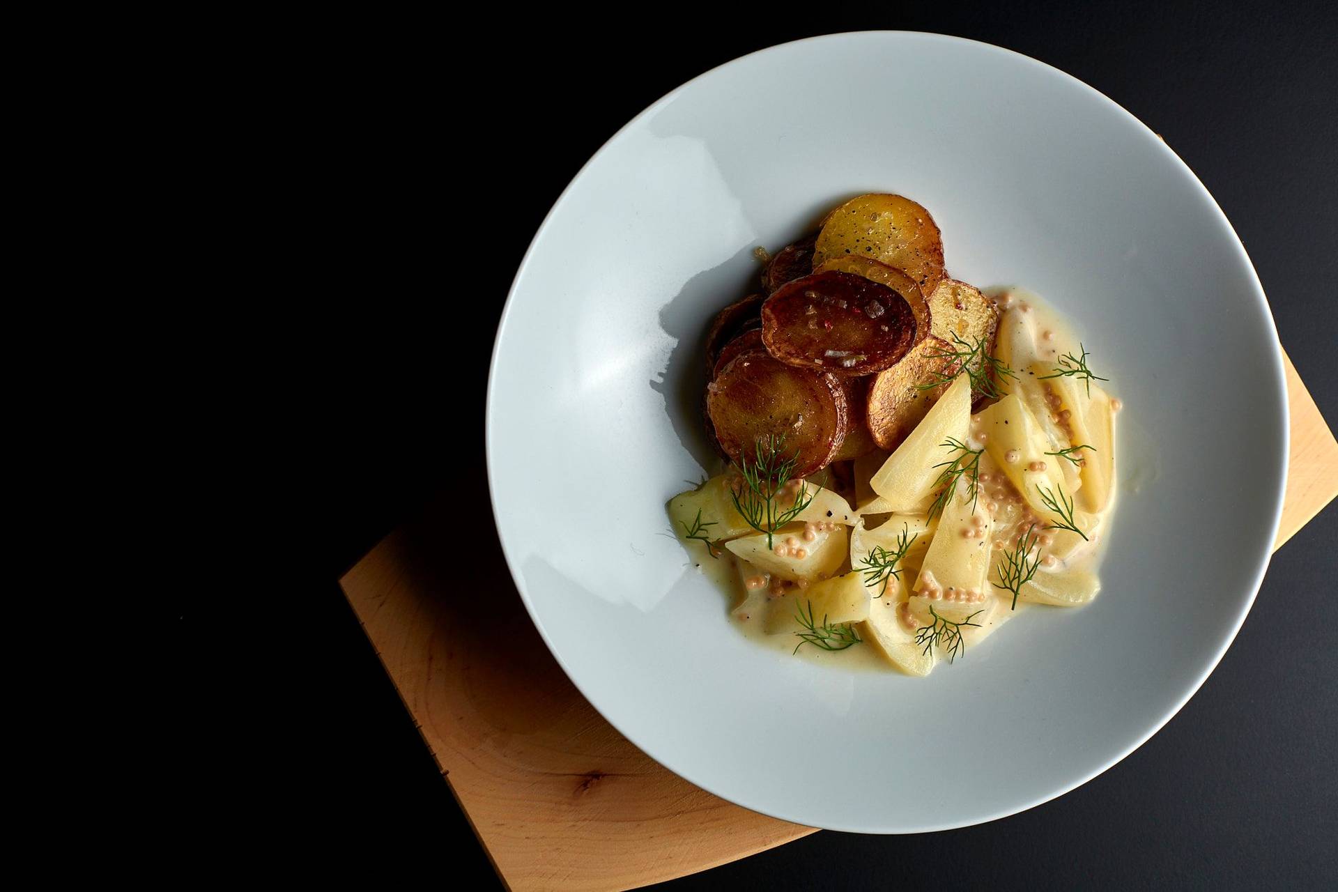 braised cucumbers with roasted potatoes in a white bowl on black background