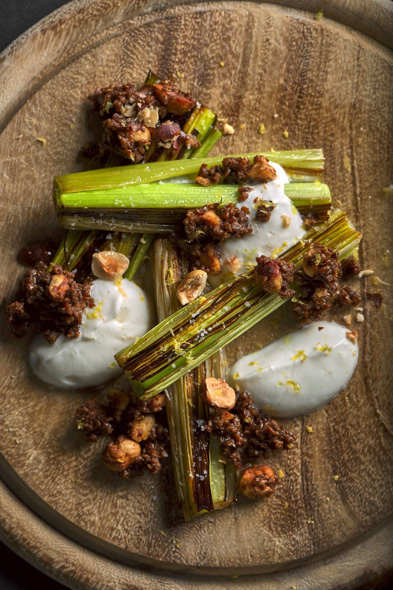 beer braised leek with pumpernickel and skyr on a wooden board with black background
