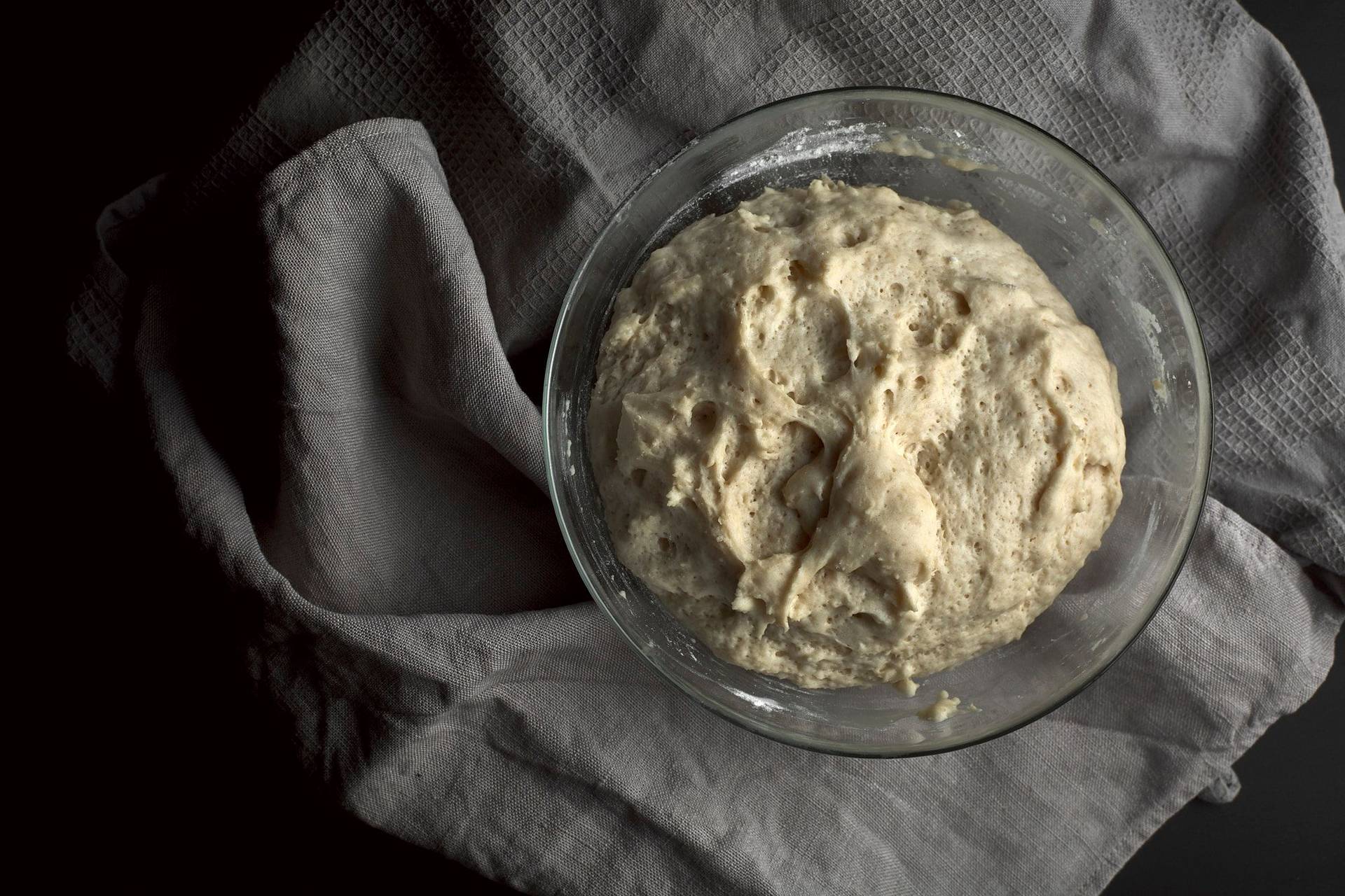 rising brioche dough with walnuts in a glass bowl on a black surface