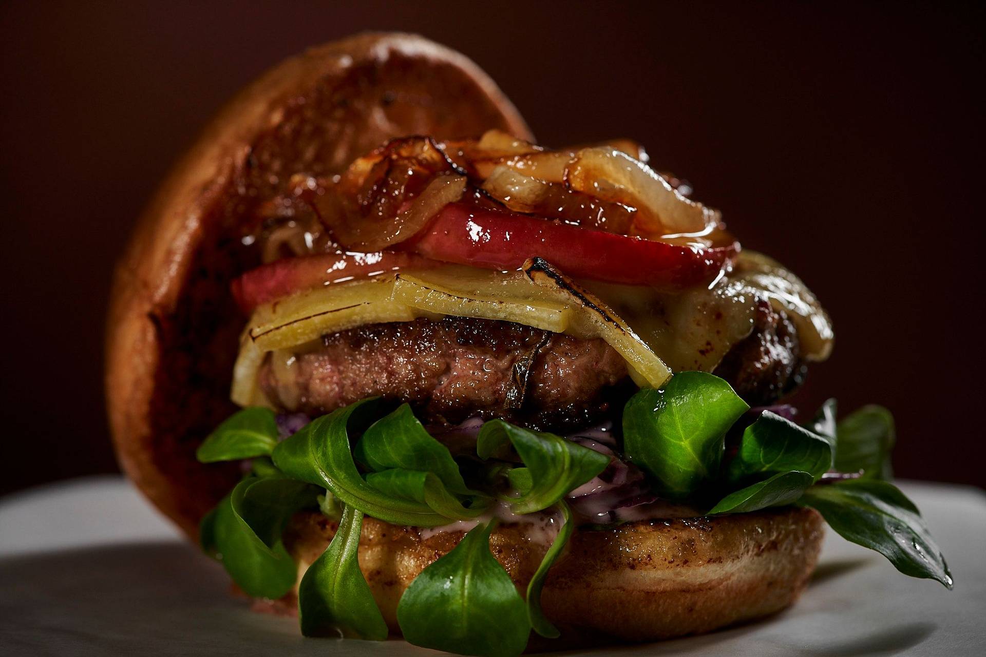 gänse burger mit rotkohl coleslaw raclette käse und karamellisiertem apfel auf holzbrett mit braunem hintergrund