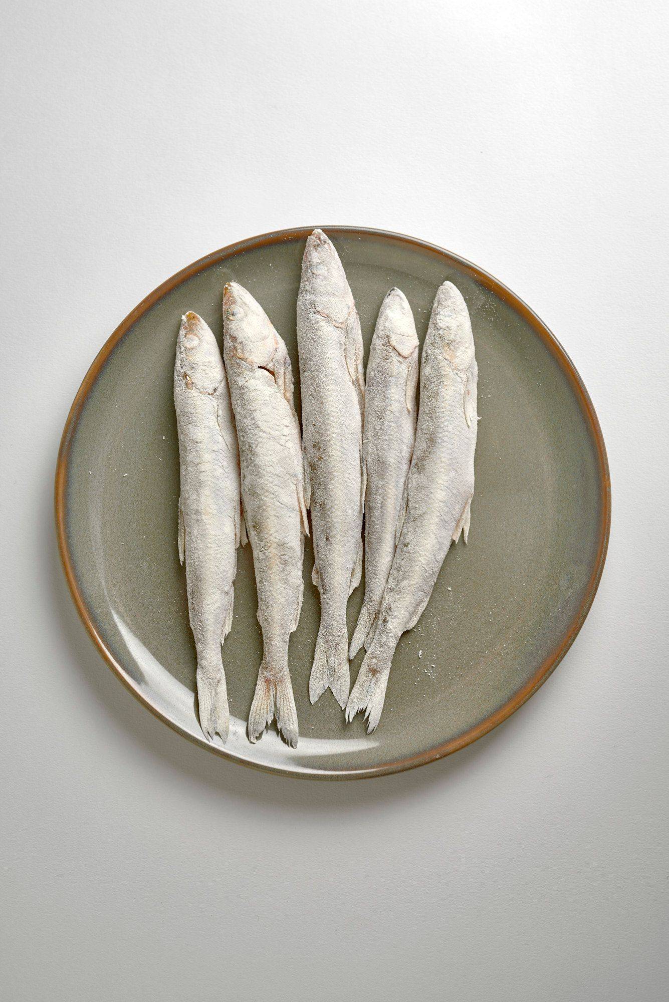 flour tossed smelt fish on a gray plate on white background
