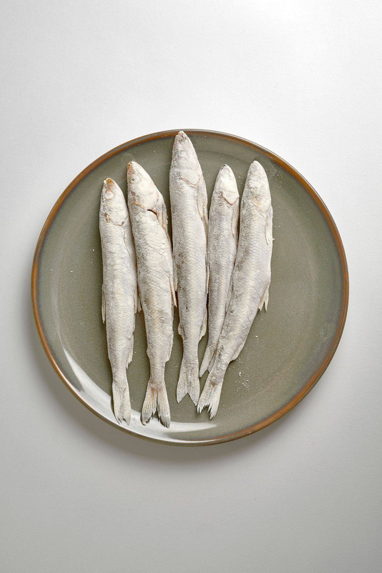floured-smelt-fish flour tossed smelt fish on a gray plate on white background
