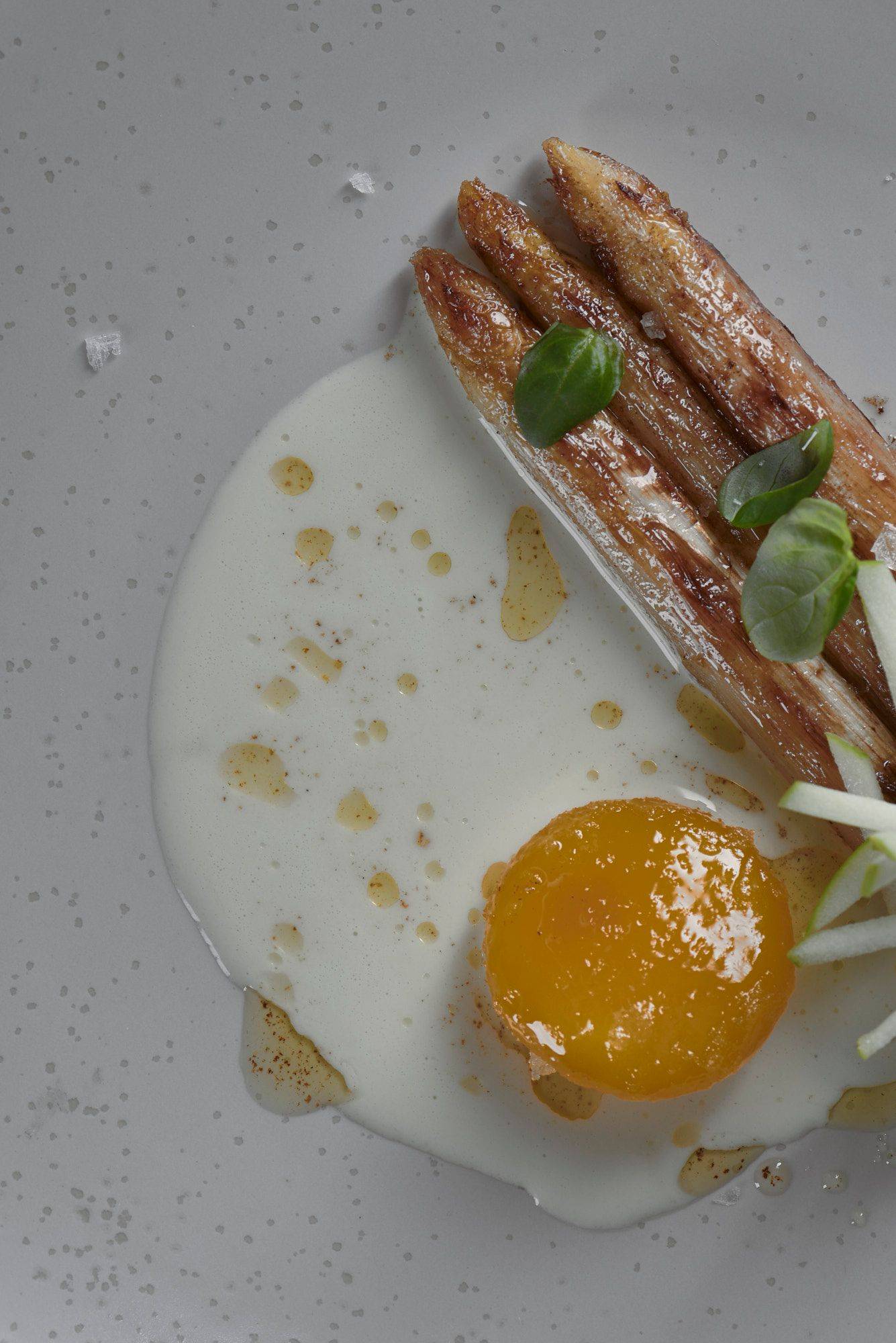 roasted white asparagus with cured egg yolk basil and green apple on a beige plate 