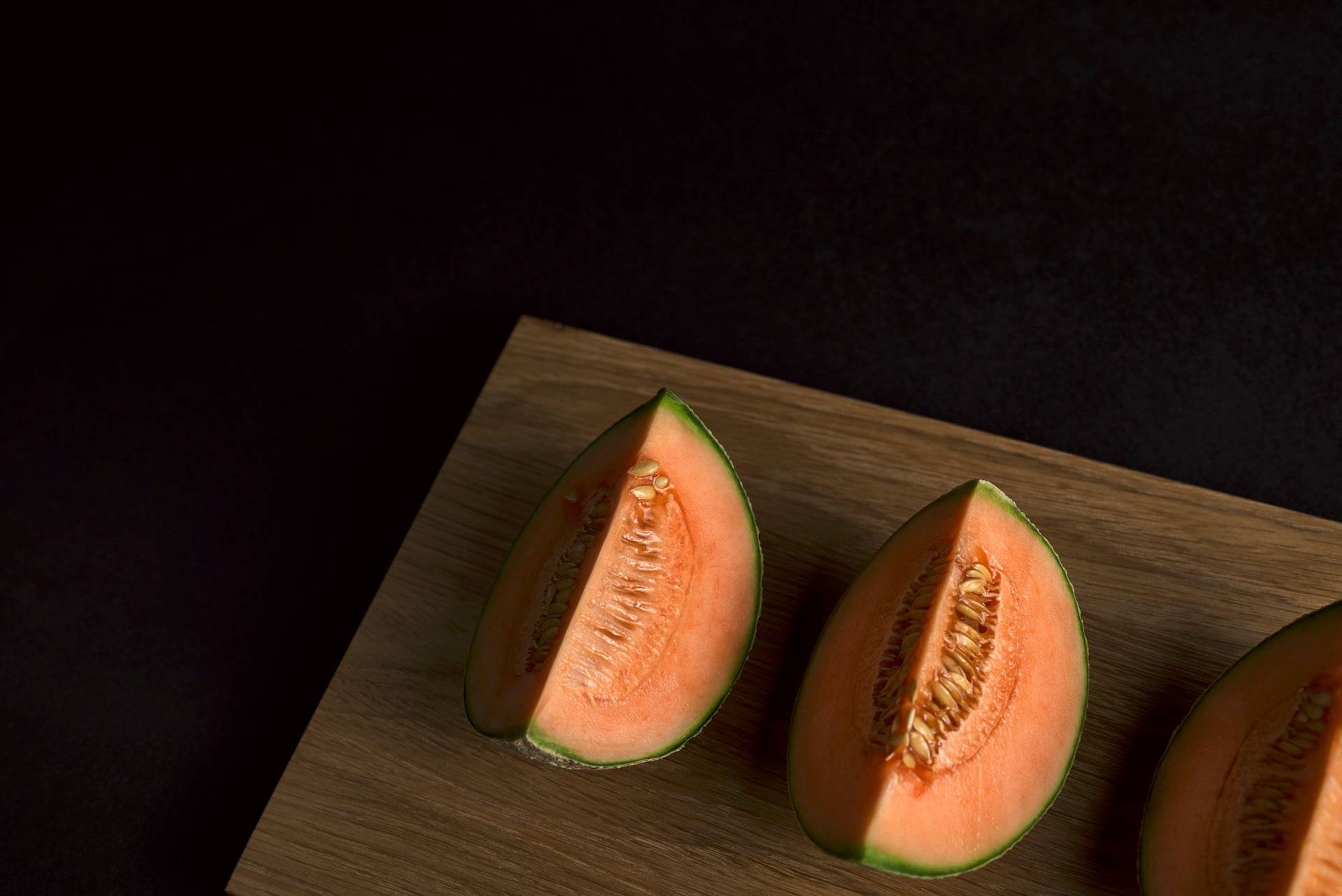 three slices of cantaloupe melon on a wooden board with black background
