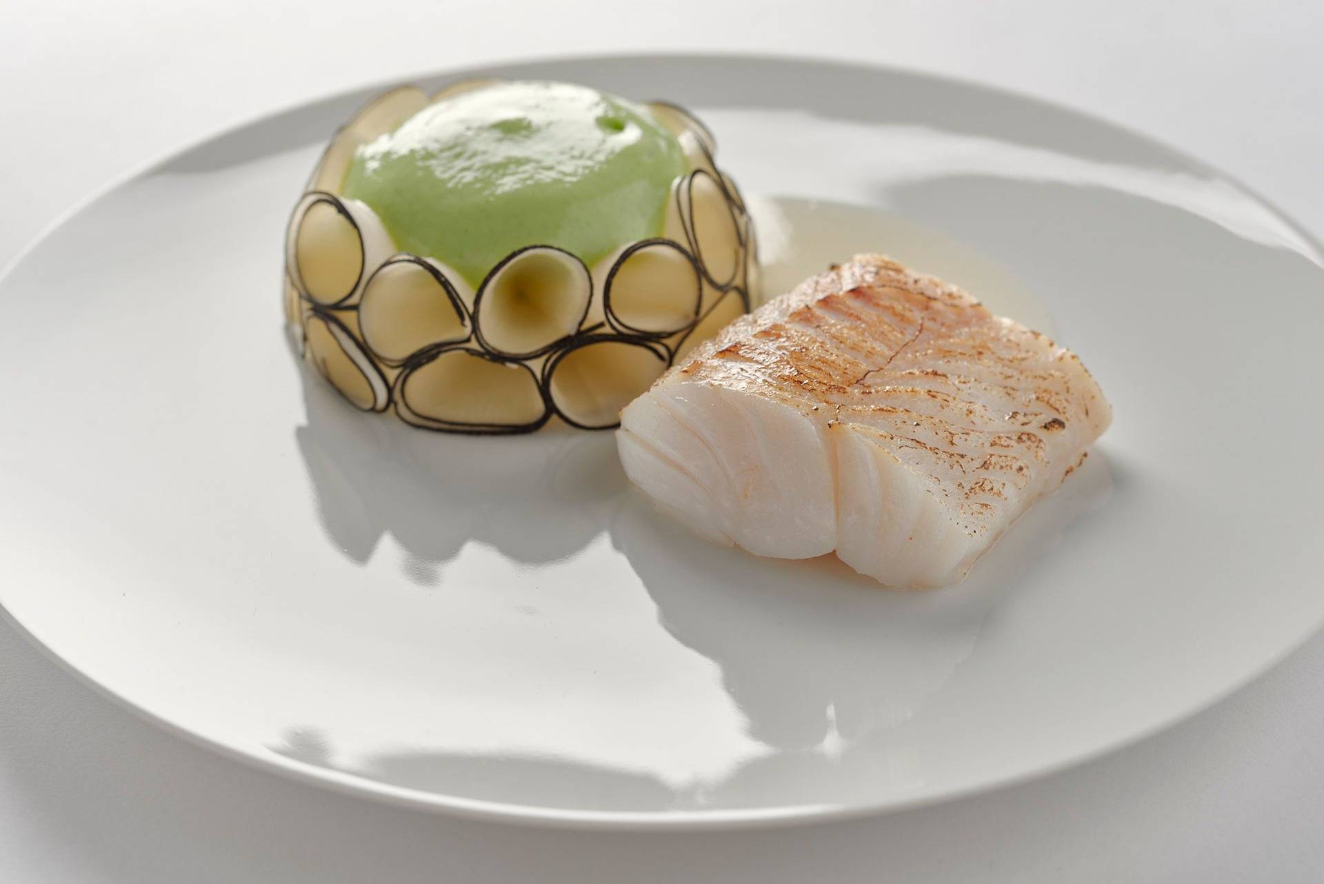 quince poached cod with black radish lovage and chardonnay on a white plate with white background