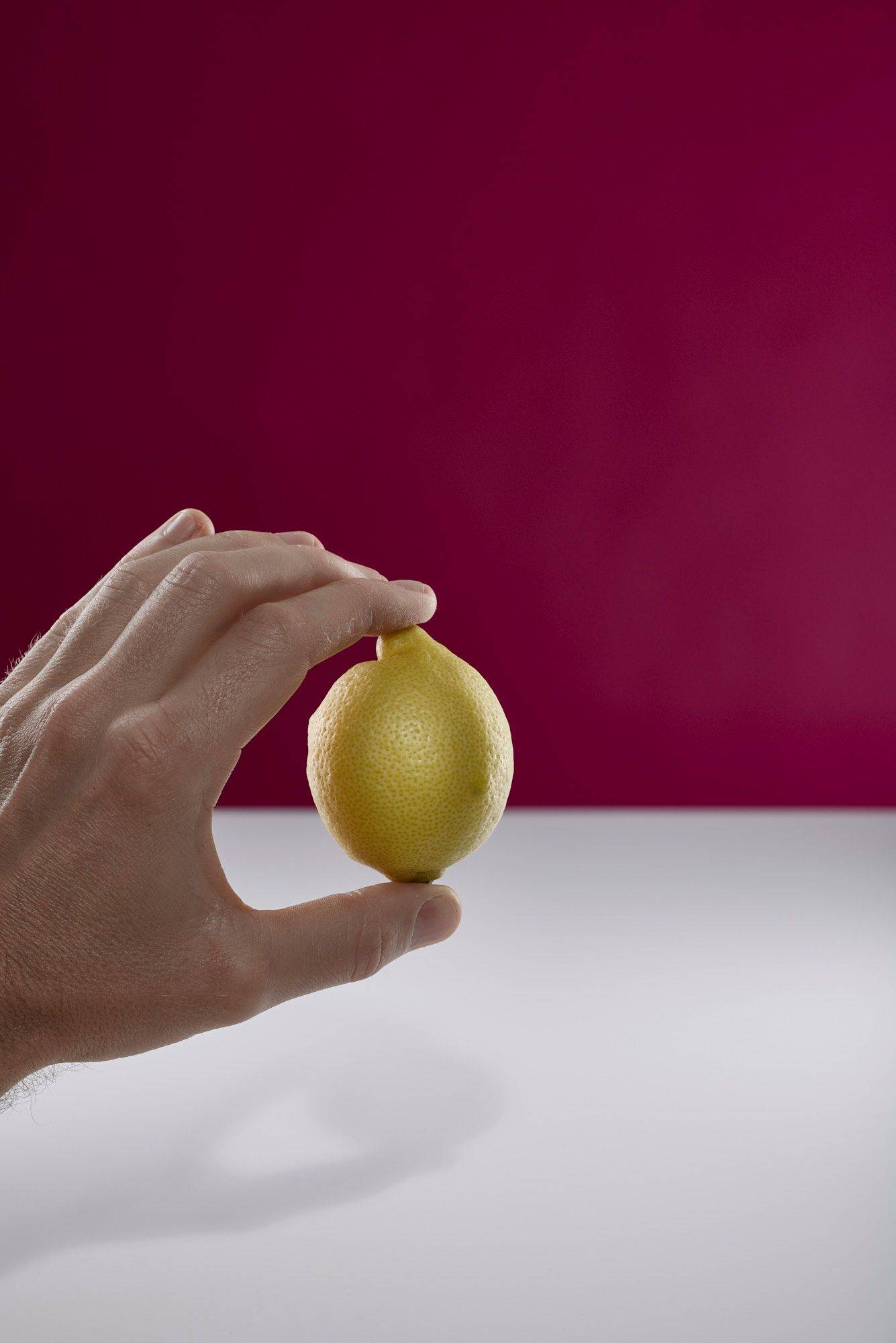 hand holding a lemon with white and pink background