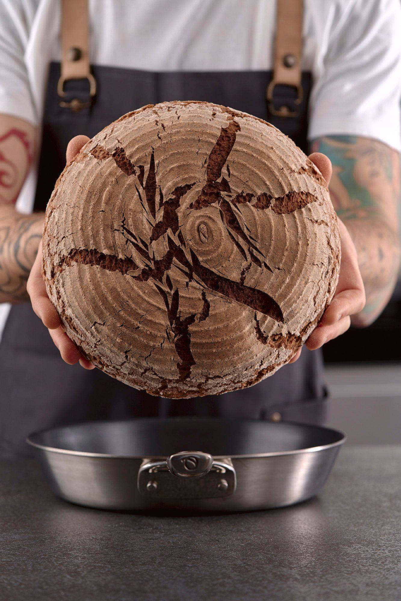 man holds a pan baked rye sourdough bread in home kitchen