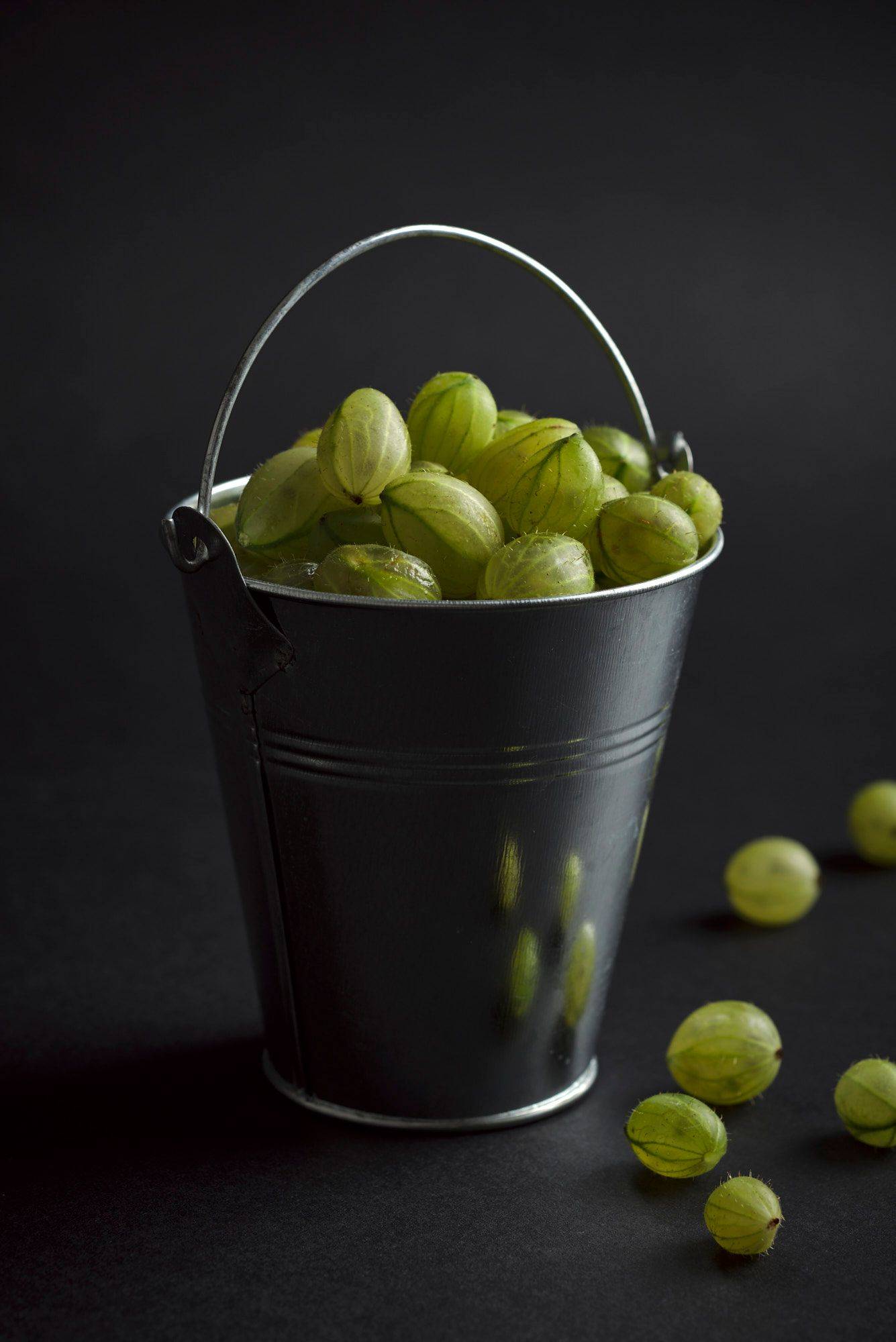 a mini bucket with gooseberriescod ceviche with gooseberries in a turquoise ceramic bowl with black background