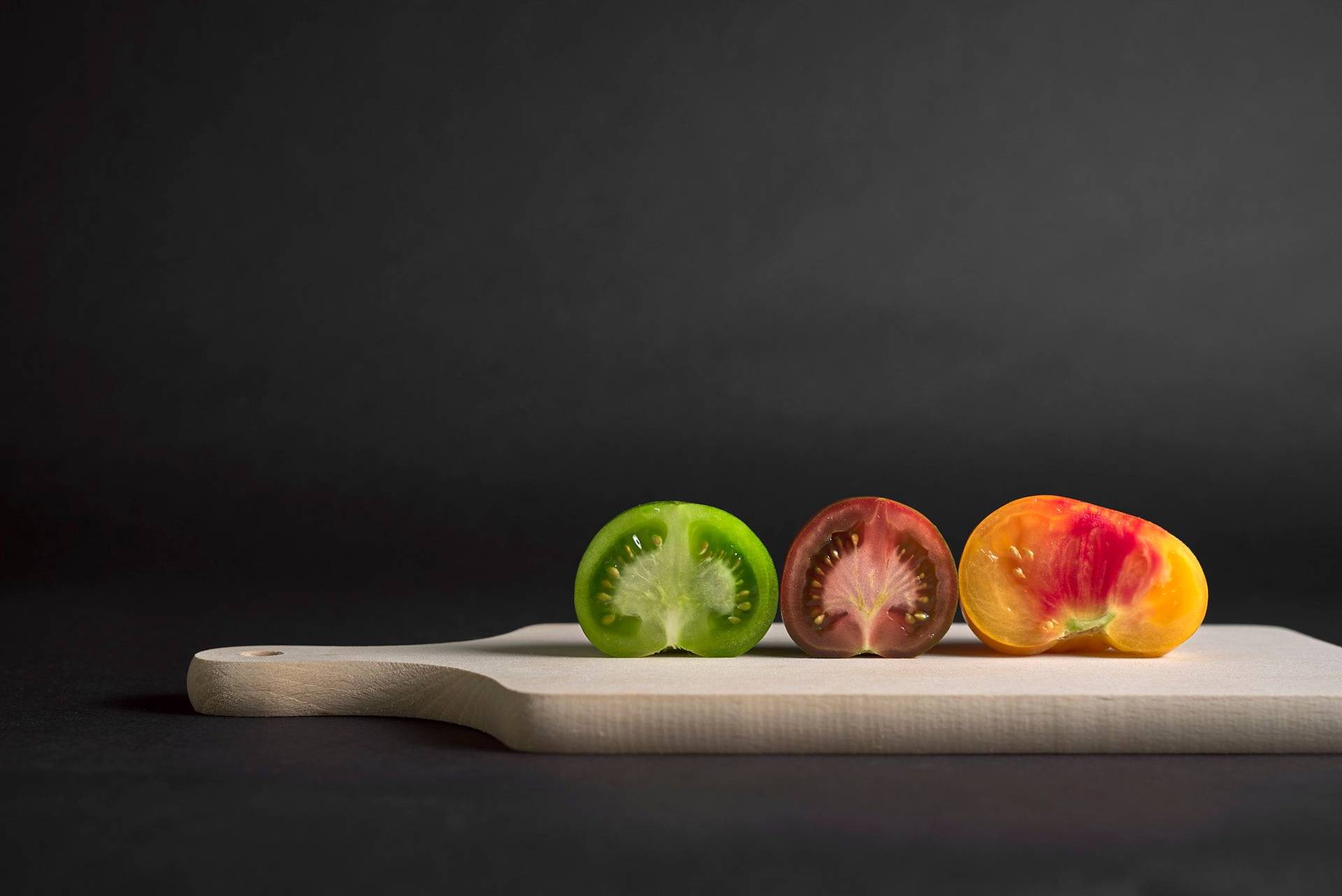 drei unterschiedliche tomaten auf einem holzbrett mit schwarzem hintergrund