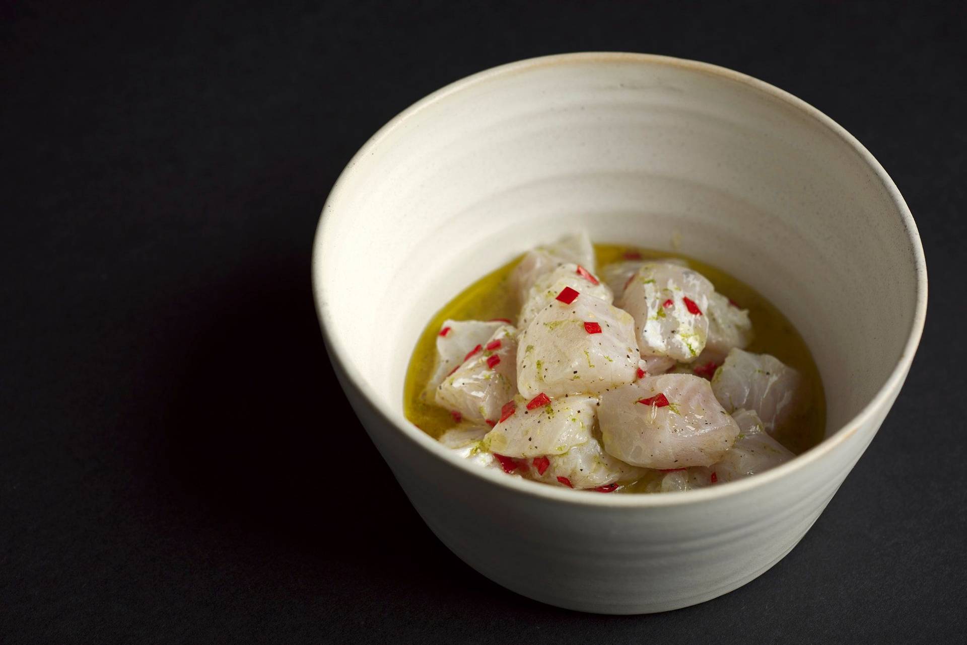 cod ceviche in a ceramic bowlcod ceviche with gooseberries in a turquoise ceramic bowl with black background