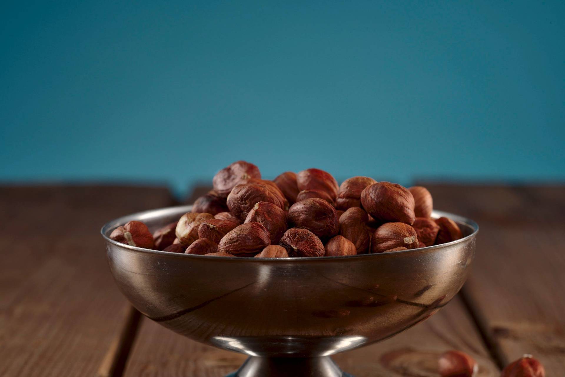 a silver bowl of hazelnuts with wooden table and blue background