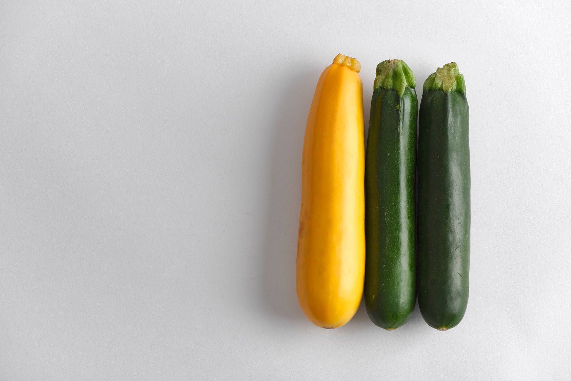one yellow and two green courgettes on a gray plate with white background