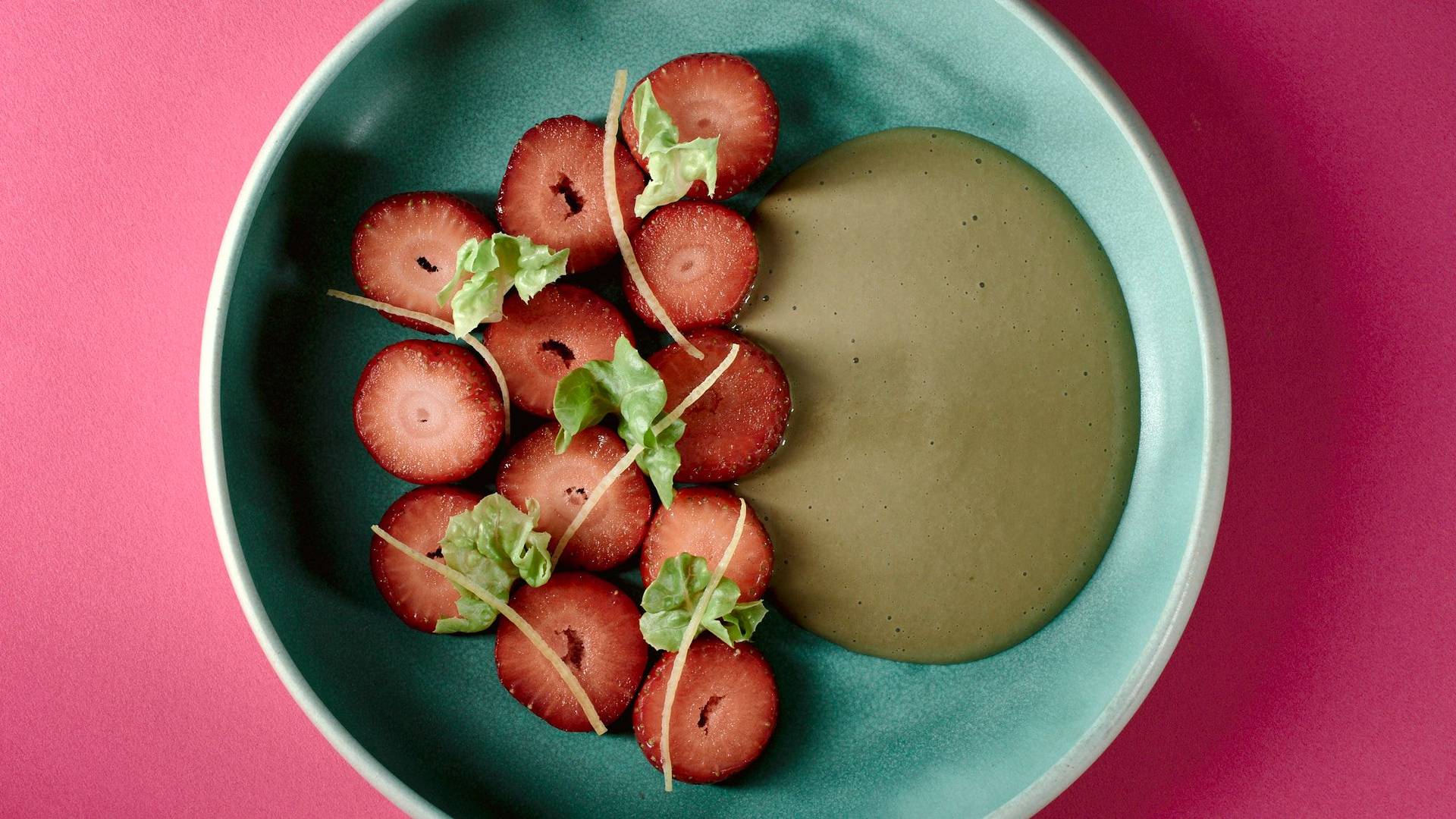 veganes erdbeerdessert mit kopfsalat und sonnenblumenkernen auf einem  türkisen teller mit pinkem hintergrund