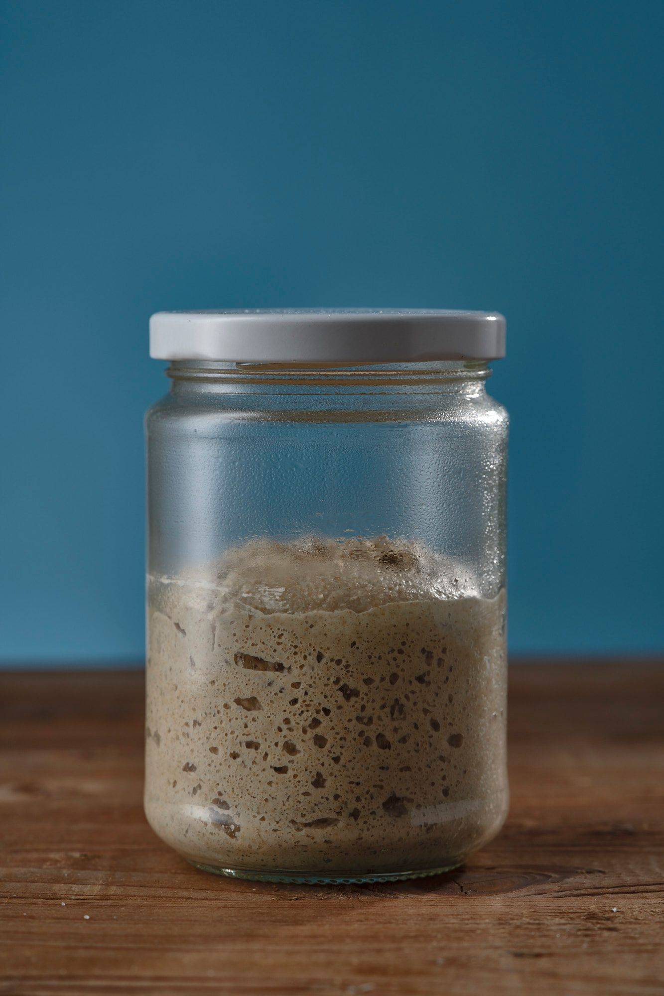 sourdough starter in a jar on a wooden table with blue background