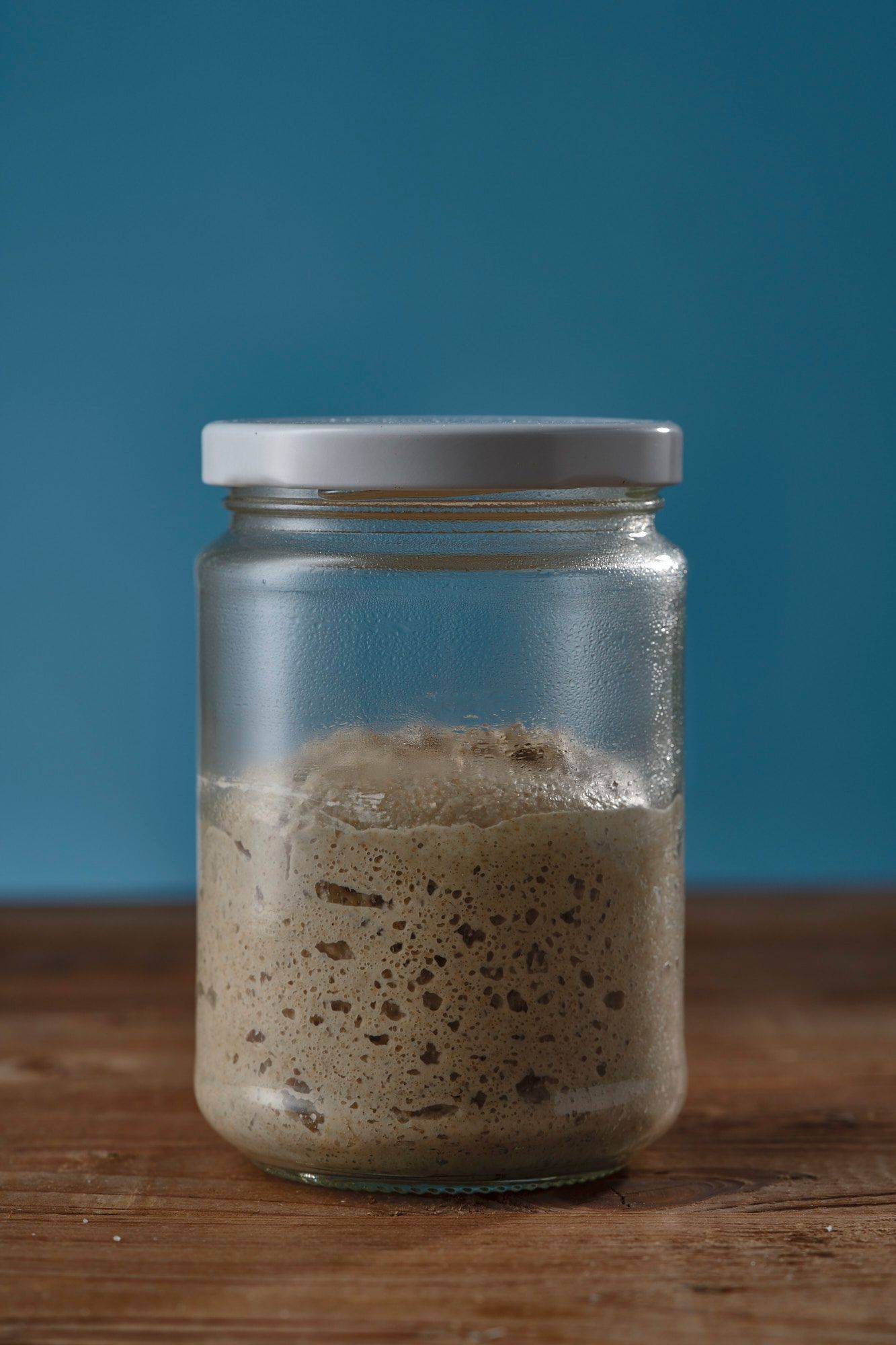 suerteig anstellgut in einem glas auf holztisch mit blauem hintergrund