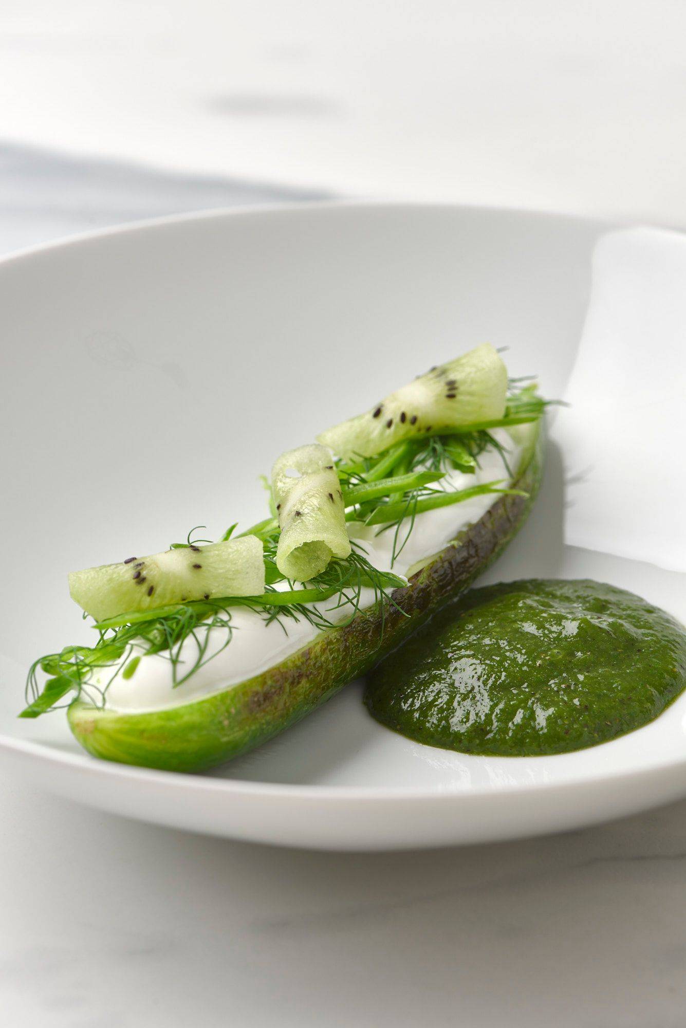 charred cucumber with kiwi salsa skyr and dill on a white plate with a marbled sapienstone top