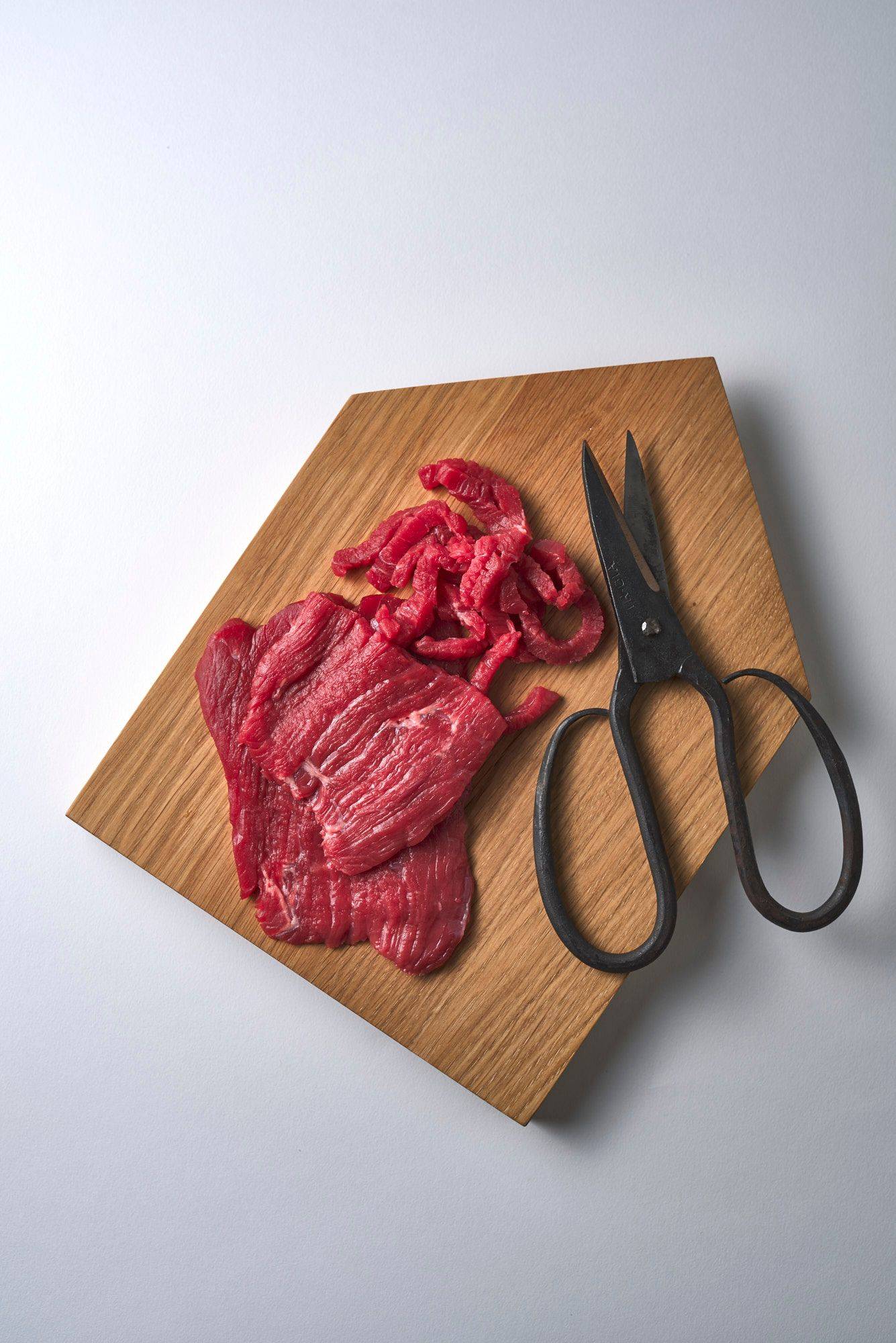 beef on a wooden tray with scissors on white background