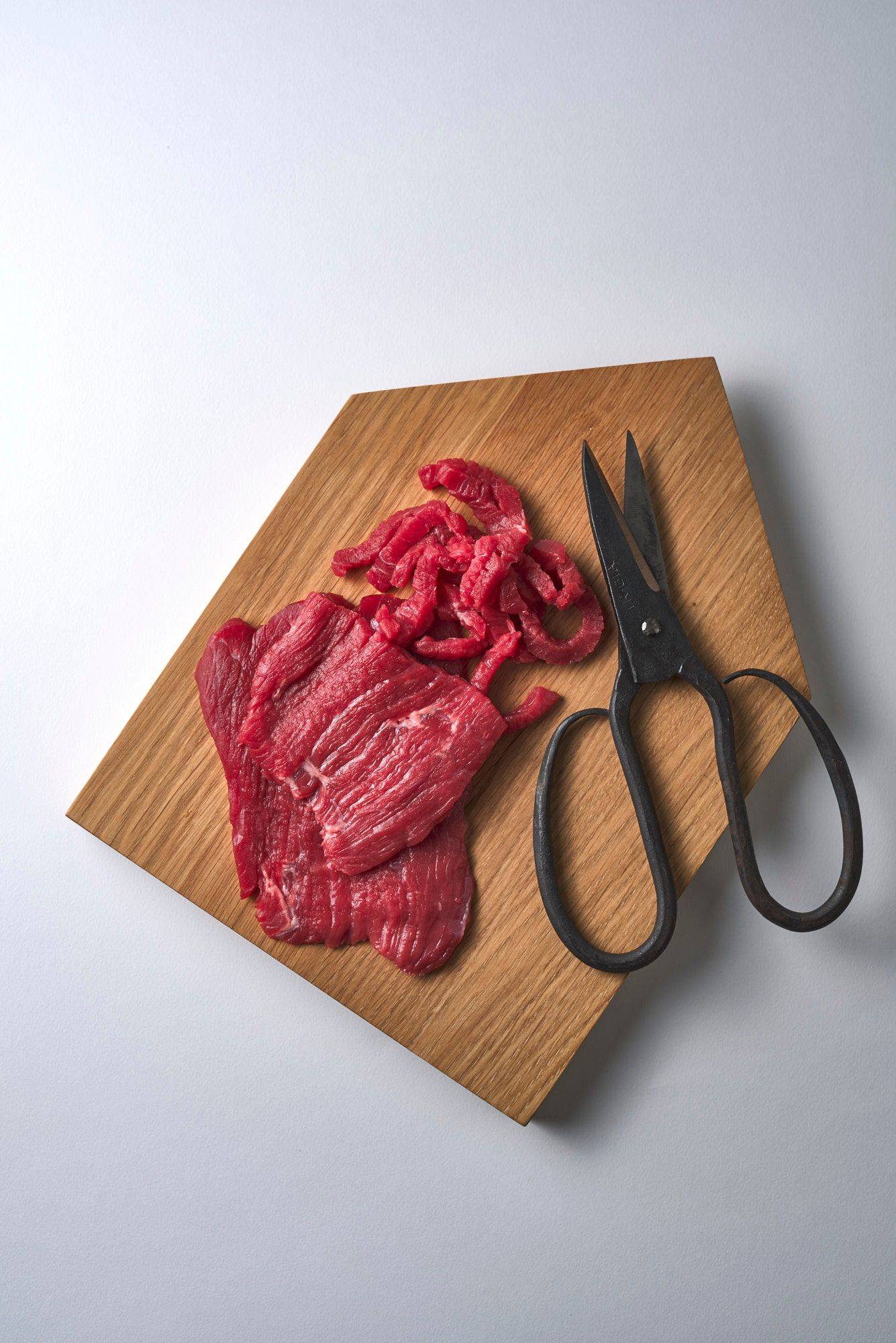 rindfleisch rohes rindfleisch auf einem holzbrett mit schere auf weißem untergrund
