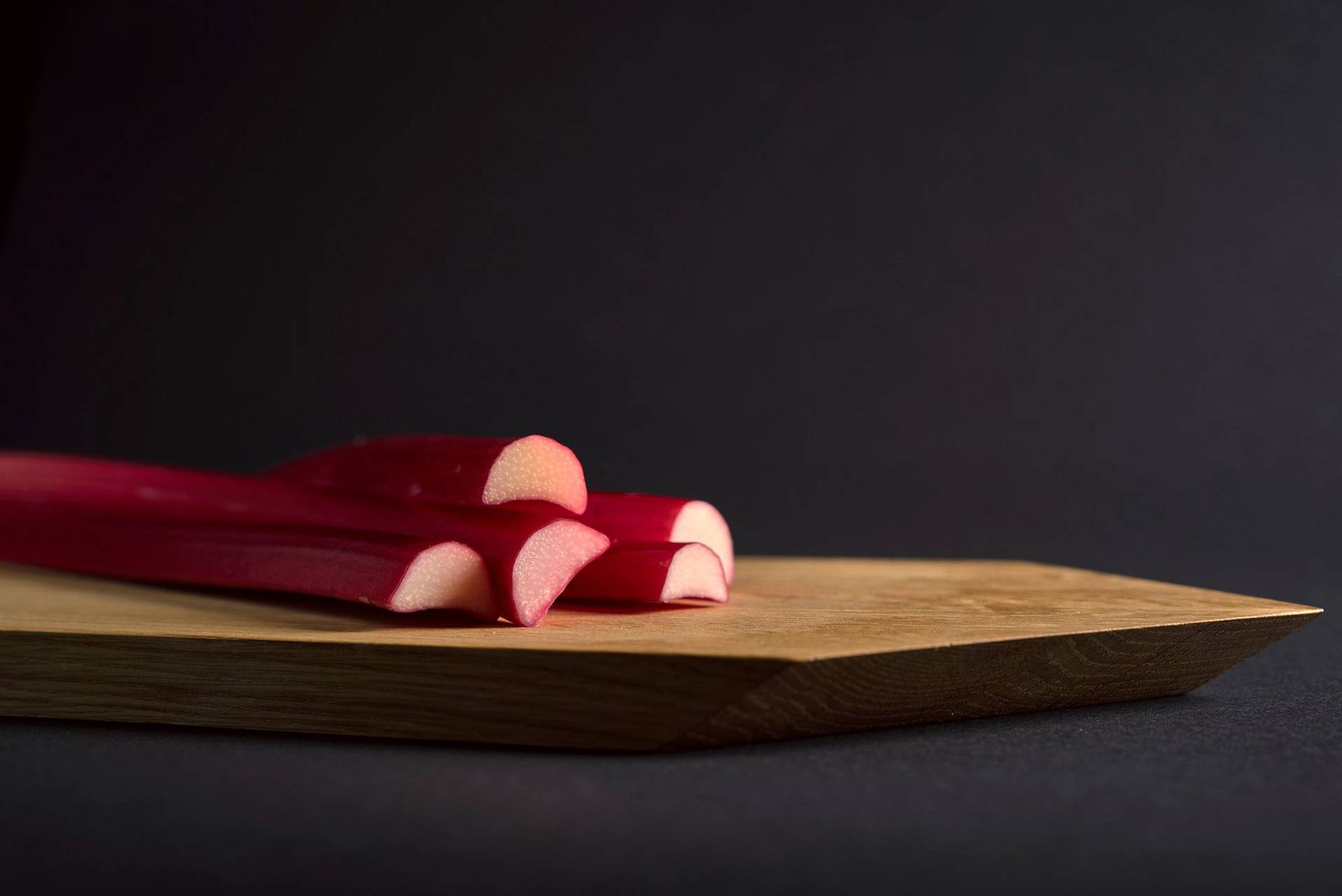 three pieces of rhubarb on a wooden board with black background