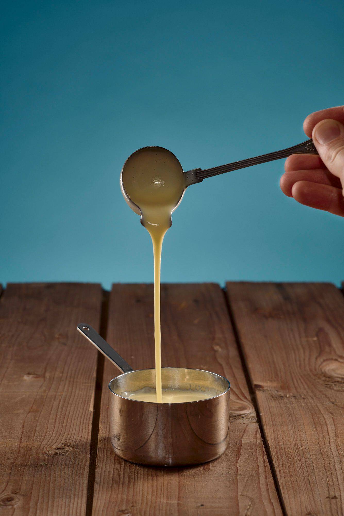 a small sauce pan with beurre blanc of pickled gherkins with wooden table and blue background
