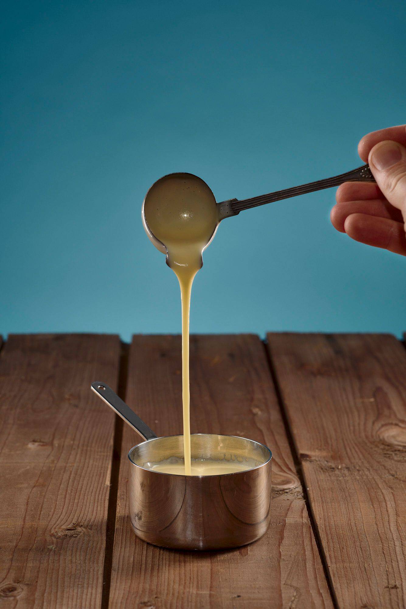 salzgurken beurre blanc in einer kleinen sauteuse mit holztisch und blauem hintergrund