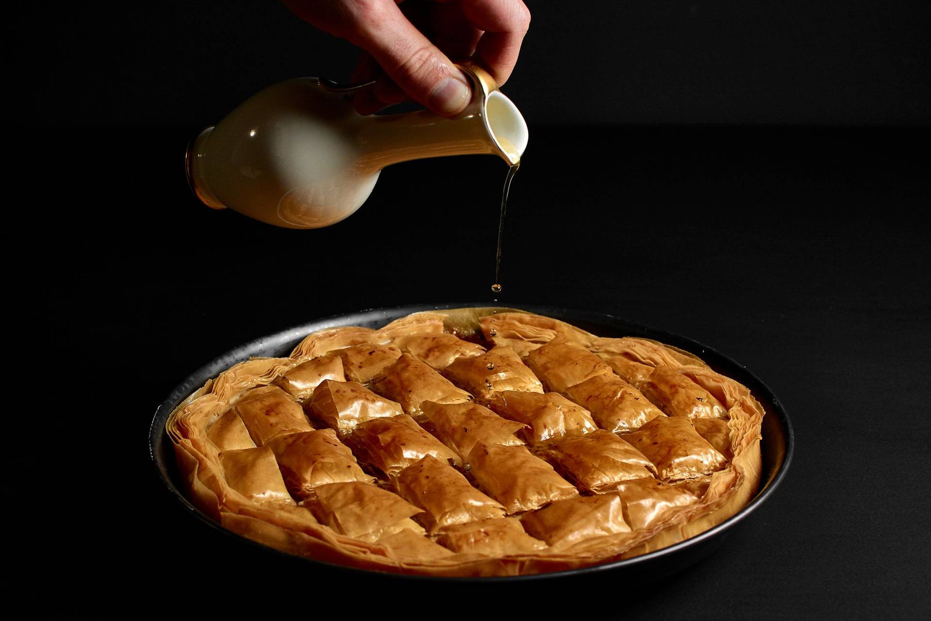 baklava mit haselnüssen und walnüssen in einer backform auf schwarzem hintergrund