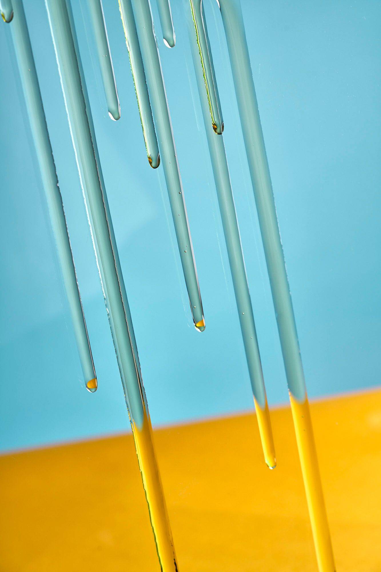olive oil running down a glass with yellow and blue background