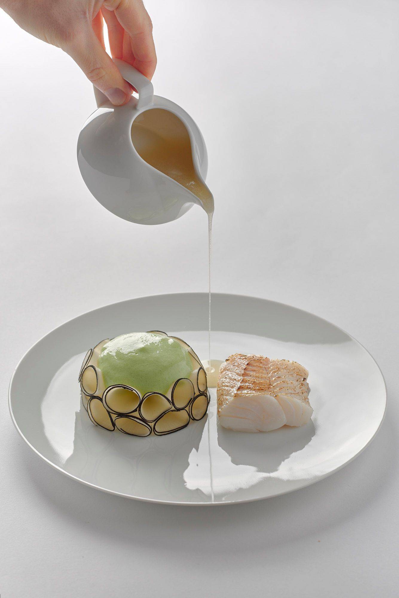 quince-poached-cod-with-black-radish-lovage-and-chardonnay quince poached cod with black radish lovage and chardonnay on a white plate with white background