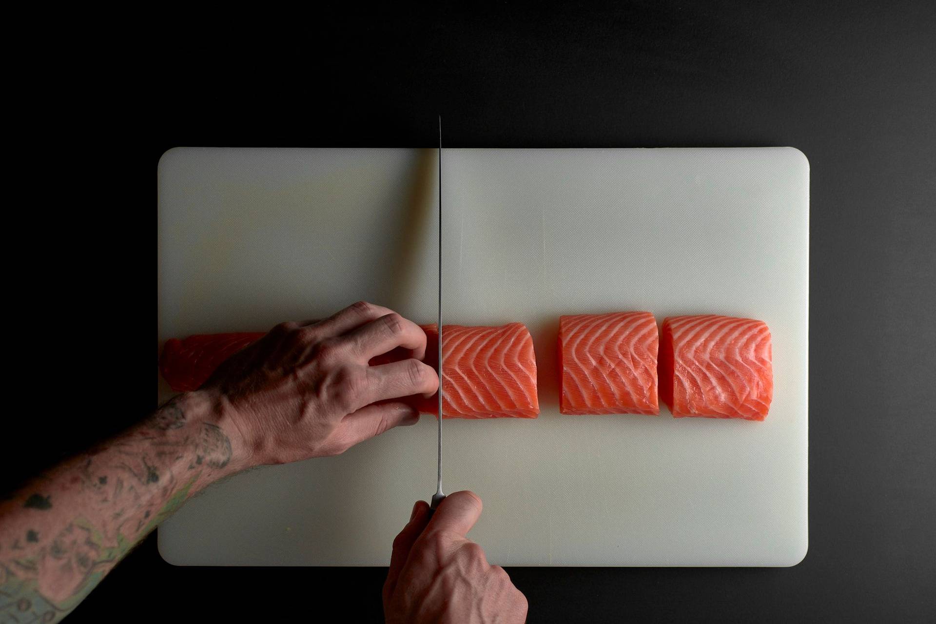 zwei hände portionieren lachs filet auf weißem brett mit schwarzem hintergrund