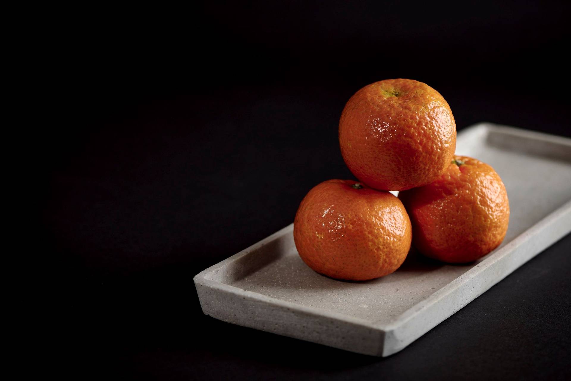 three tangerines on a concrete plate with black background