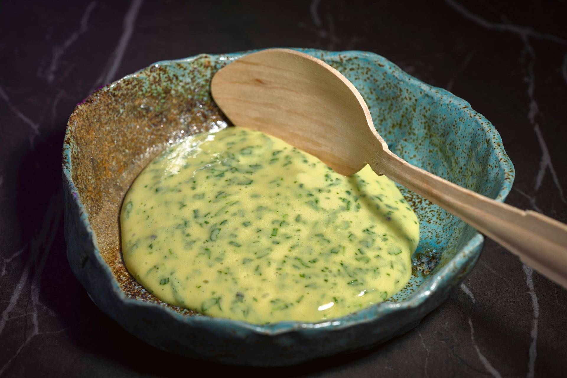 homemade terragon mayonnaise in a turquoise ceramic bowl with wooden spoon on a gray marbled sapienstone top 
