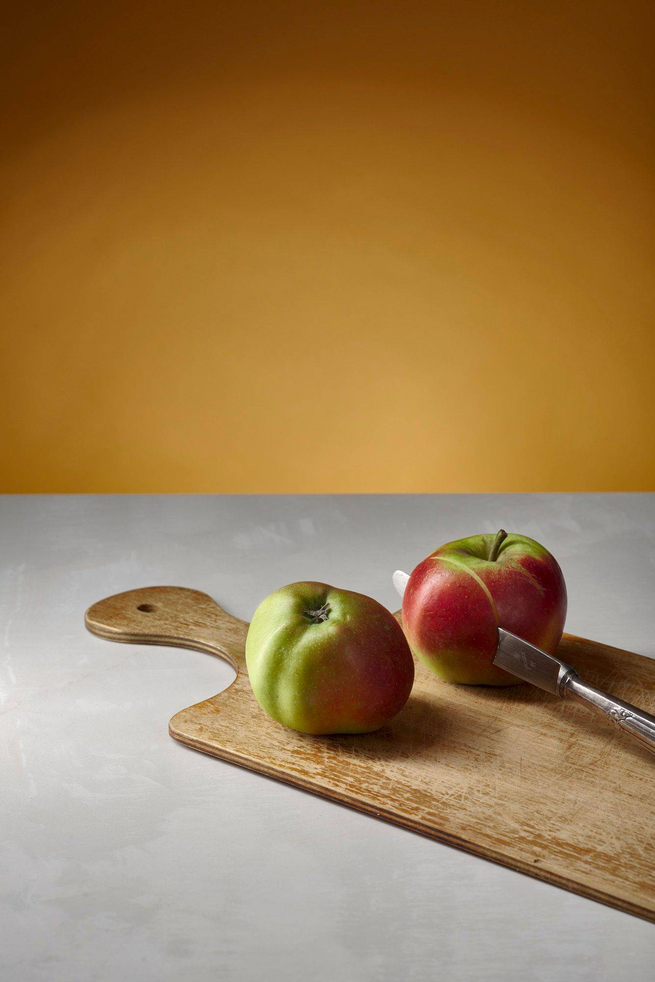 two red apples on a wooden board with white sapienstone top and yellow background