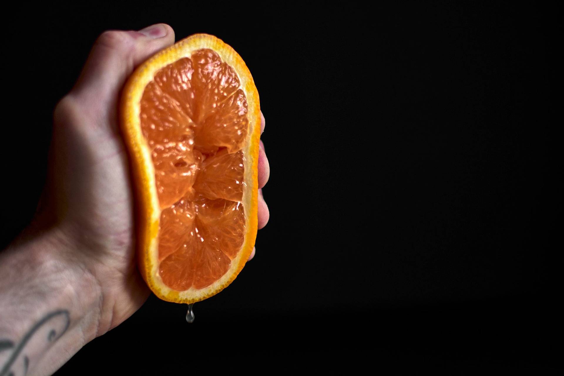 eine hand presst eine orange aus vor schwarzem hintergrund