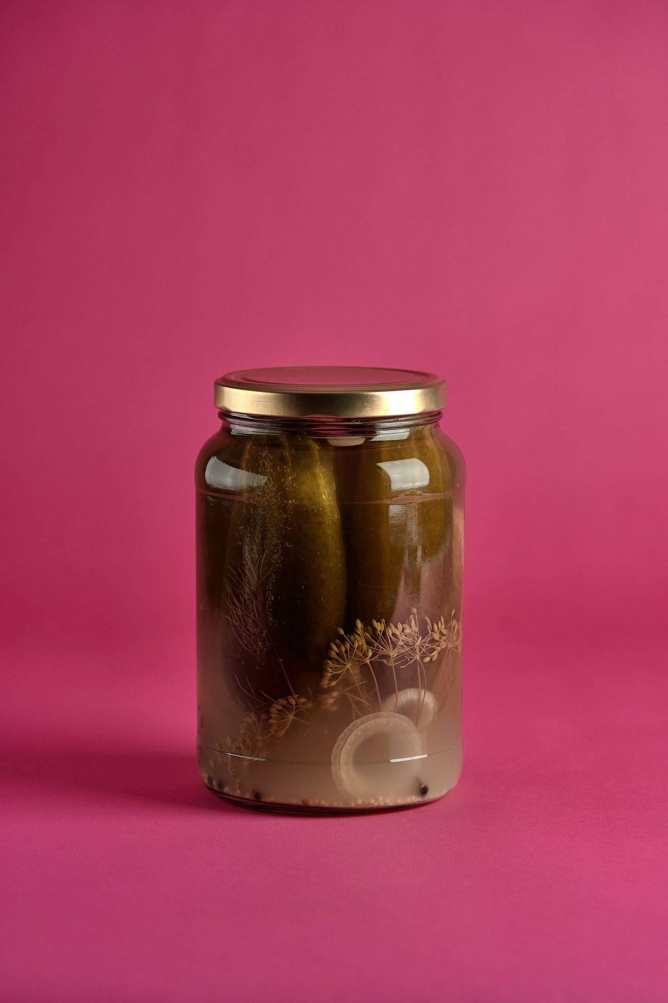 a jar of cucumber pickles on pink background