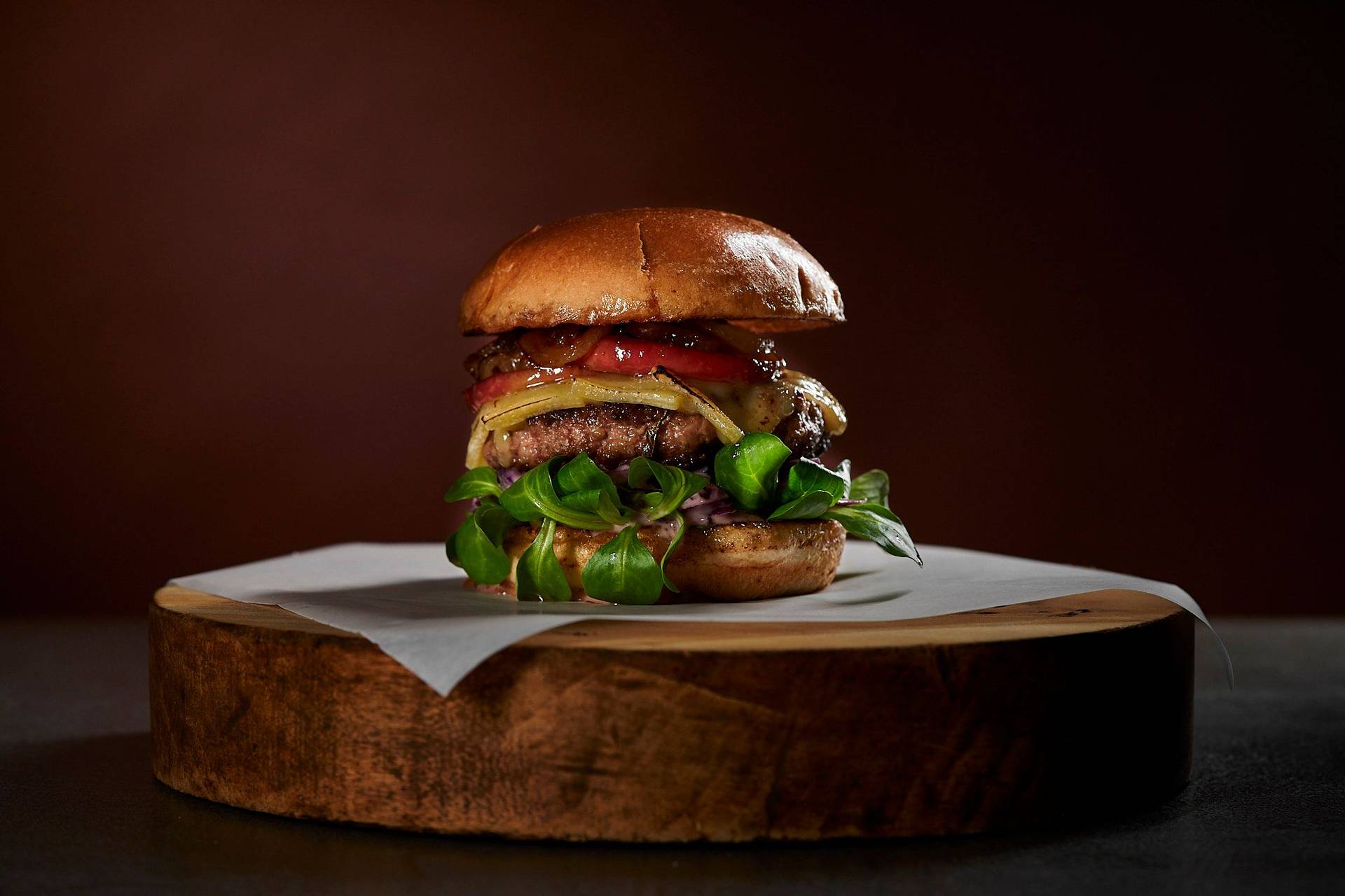 goose burger with red cabbage coleslaw raclette cheese and caramelized apple on a wooden board with brown background