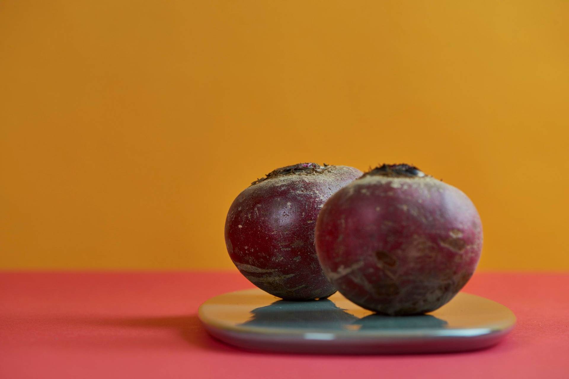 two bulbs of beetroot on a gray plate with red and yellow background