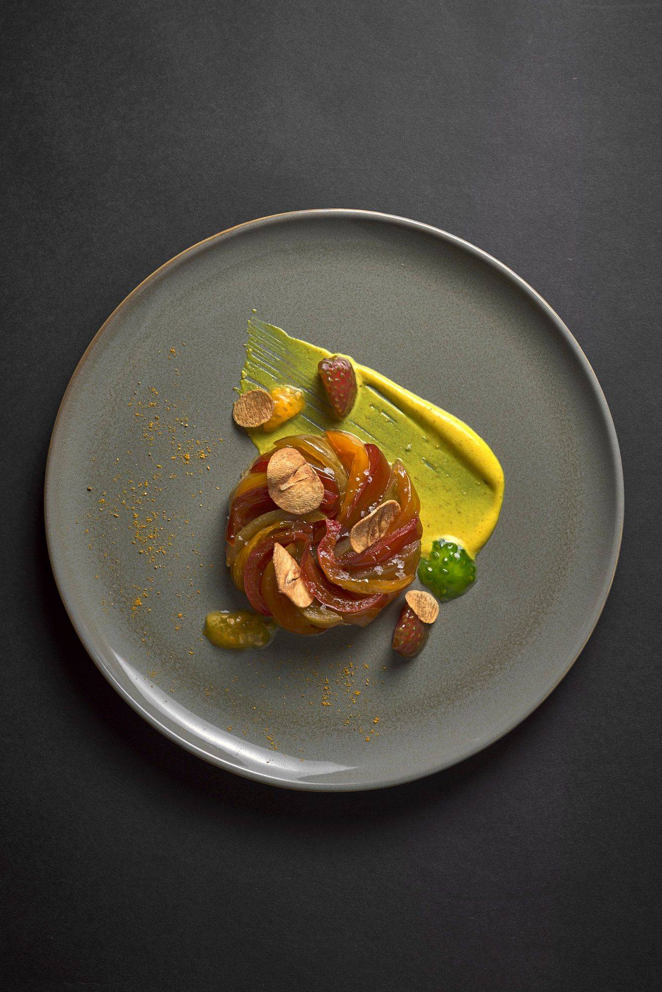 savory tomato tarte tatin with curry creme fraiche and garlic crisps on a gray plate with black background